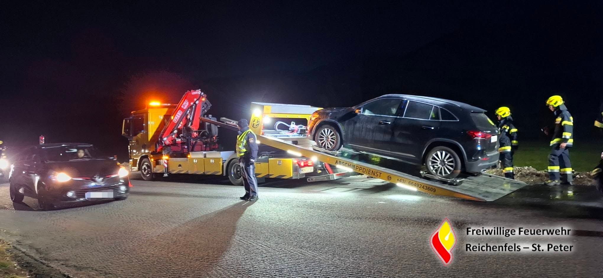 Abschleppwagen lädt Auto nach Motorbrand, Feuerwehrleute mit Helmen sind im Einsatz.
