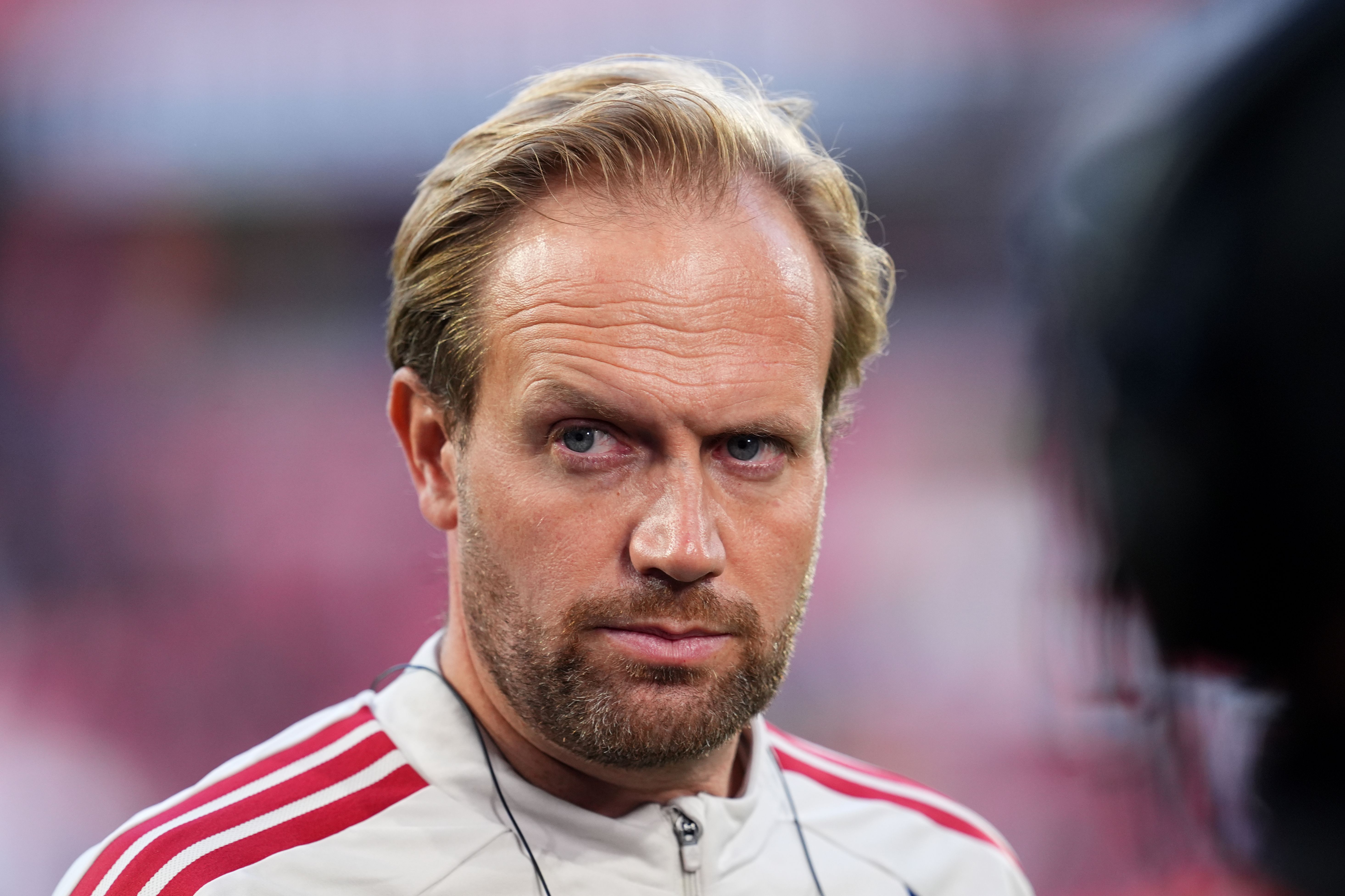 Ein Mann im Trainingsanzug blickt ernsthaft in die Kamera, unscharfer Hintergrund.