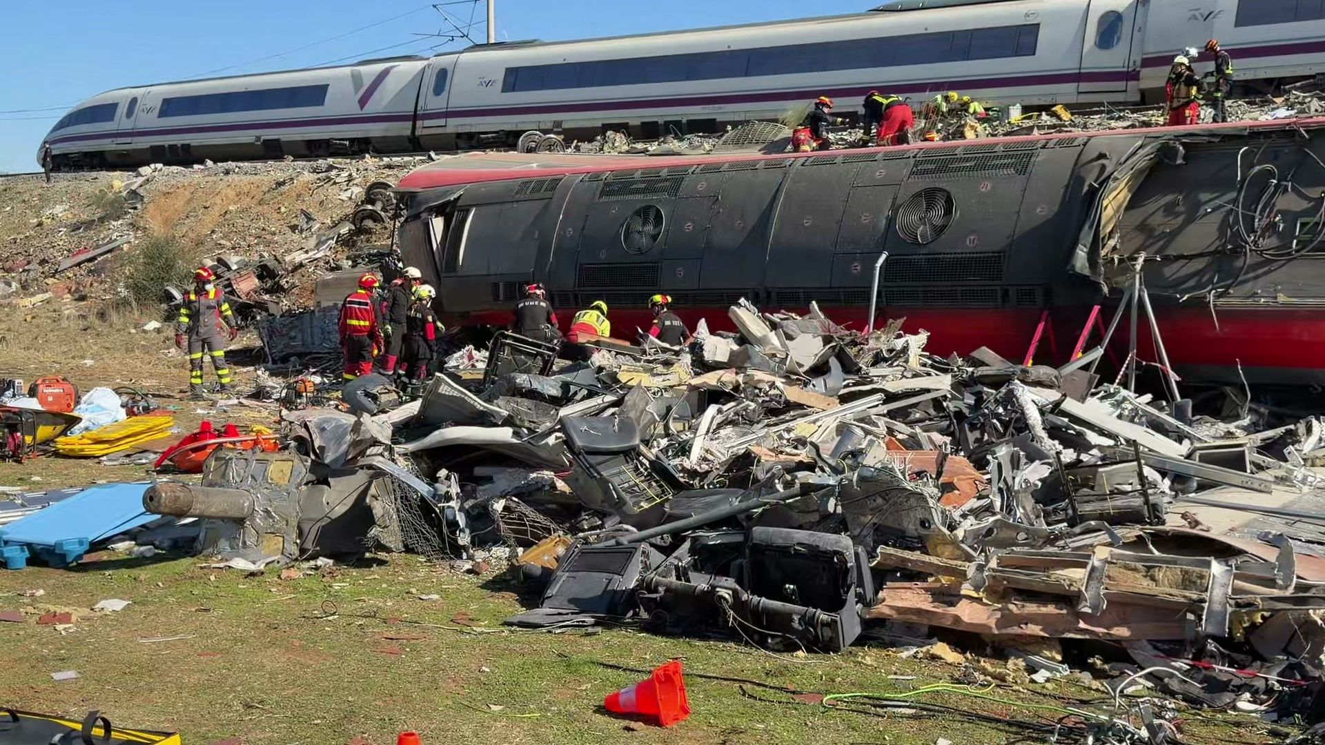 Rettungskräfte arbeiten an der Unfallstelle mit umgestürzten Zügen und Trümmern nach einem Zugunglück.