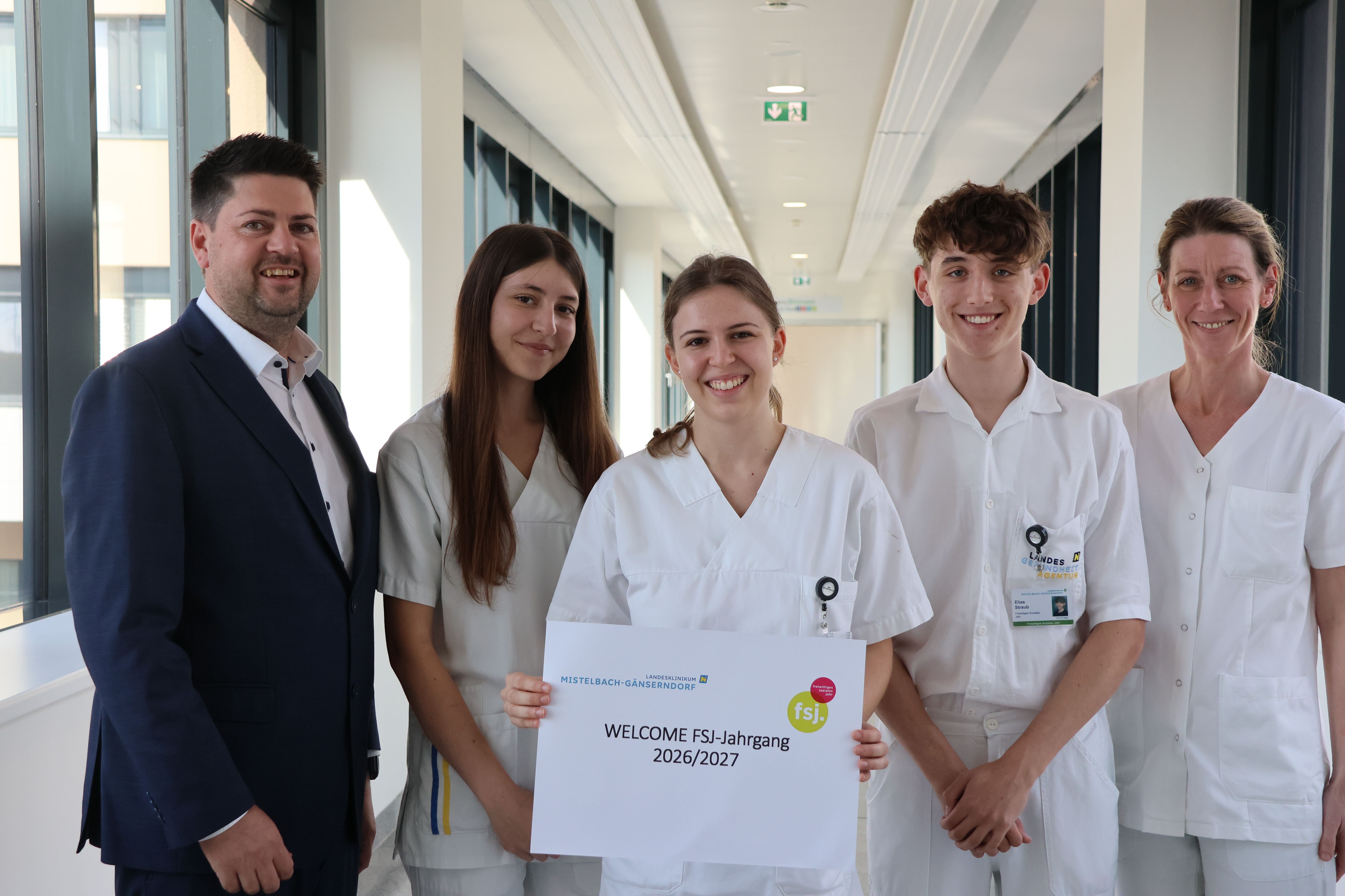 Fünf Personen, darunter drei in weißer Dienstkleidung, halten ein Schild "WELCOME FSJ-Jahrgang 2026/2027".
