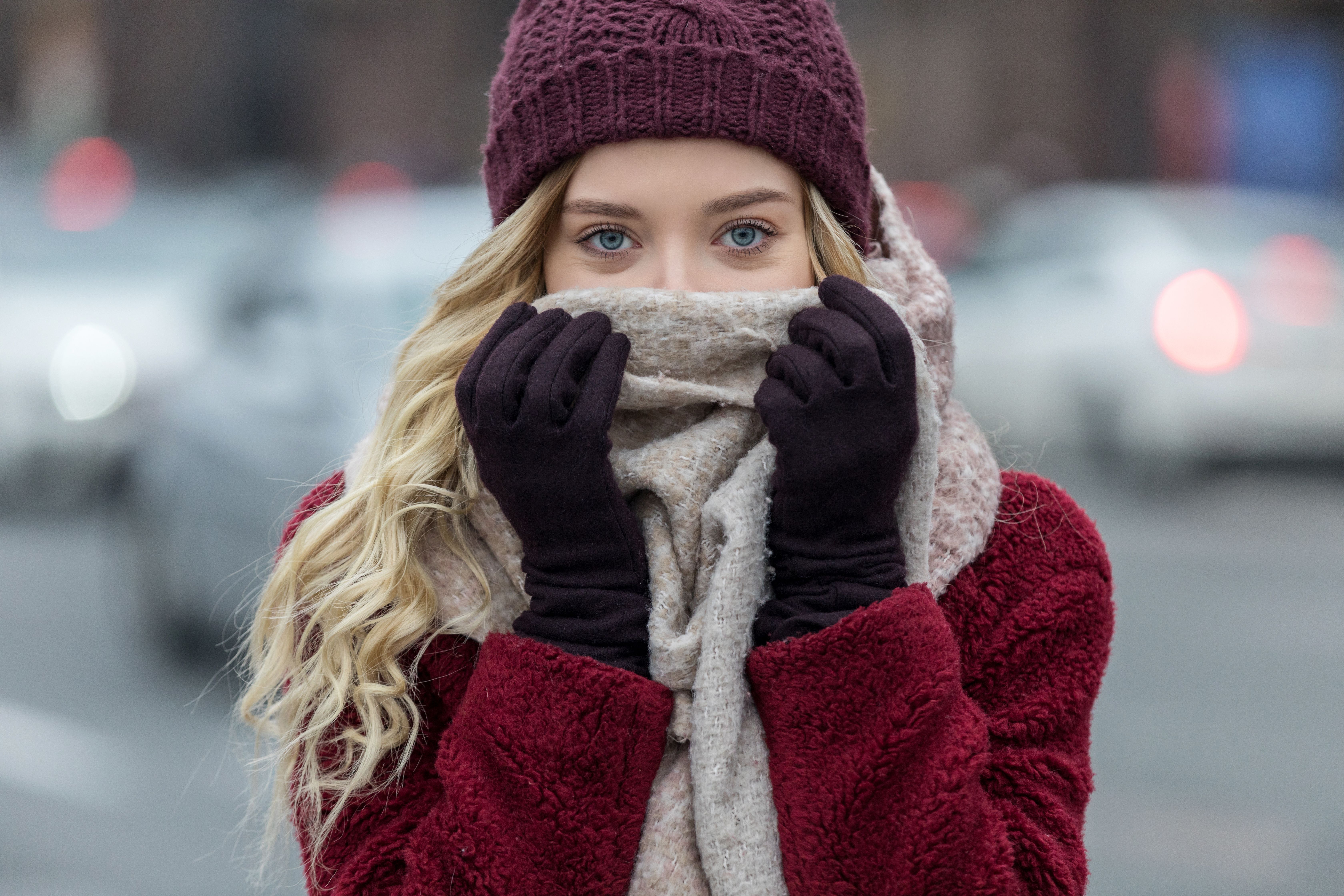 Junge Frau mit Mütze, Handschuhen und Schal schützt sich vor Kälte im Winter.