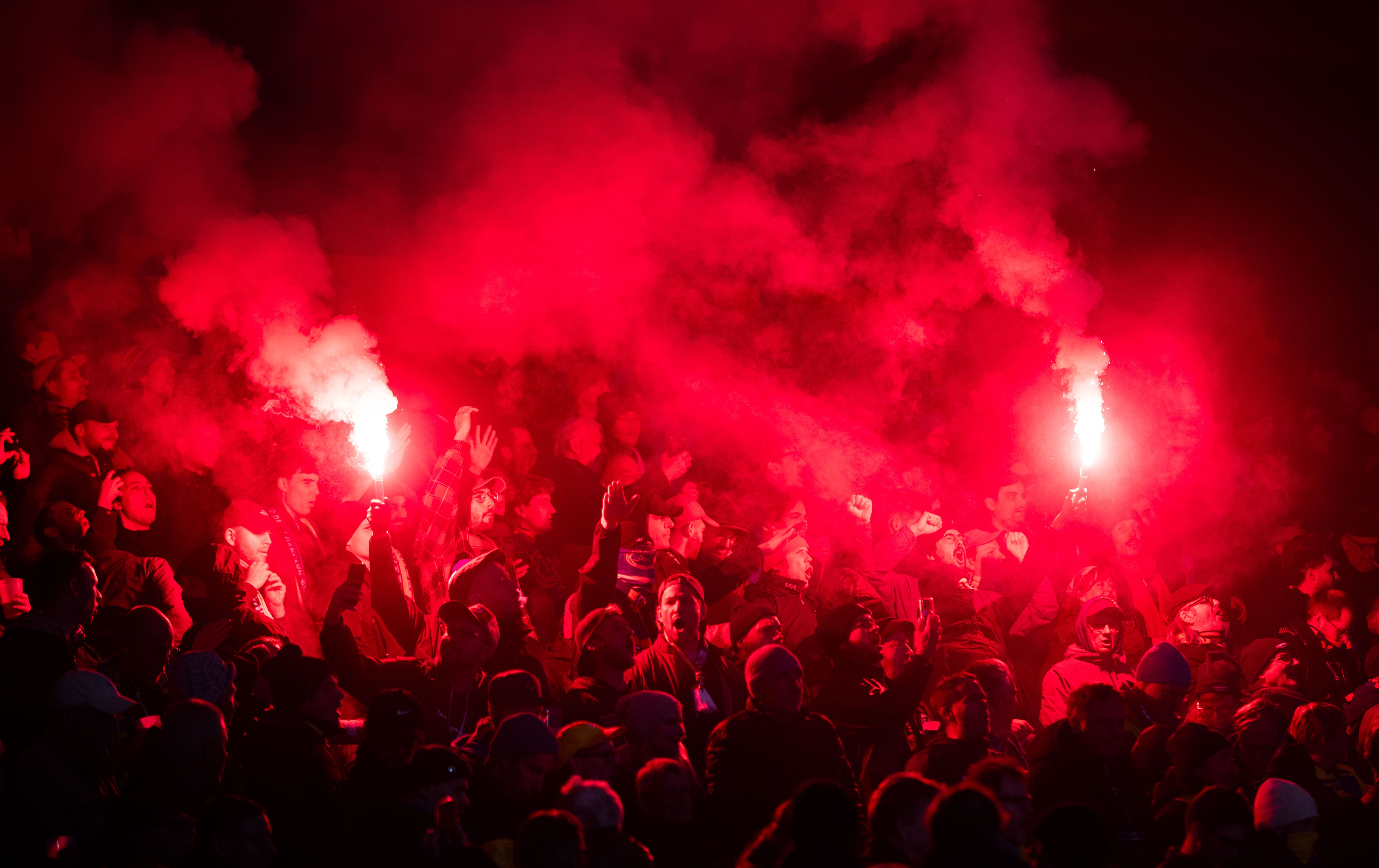 Fans zünden rote Fackeln und jubeln während eines Fußballspiels im Stadion in Wien.