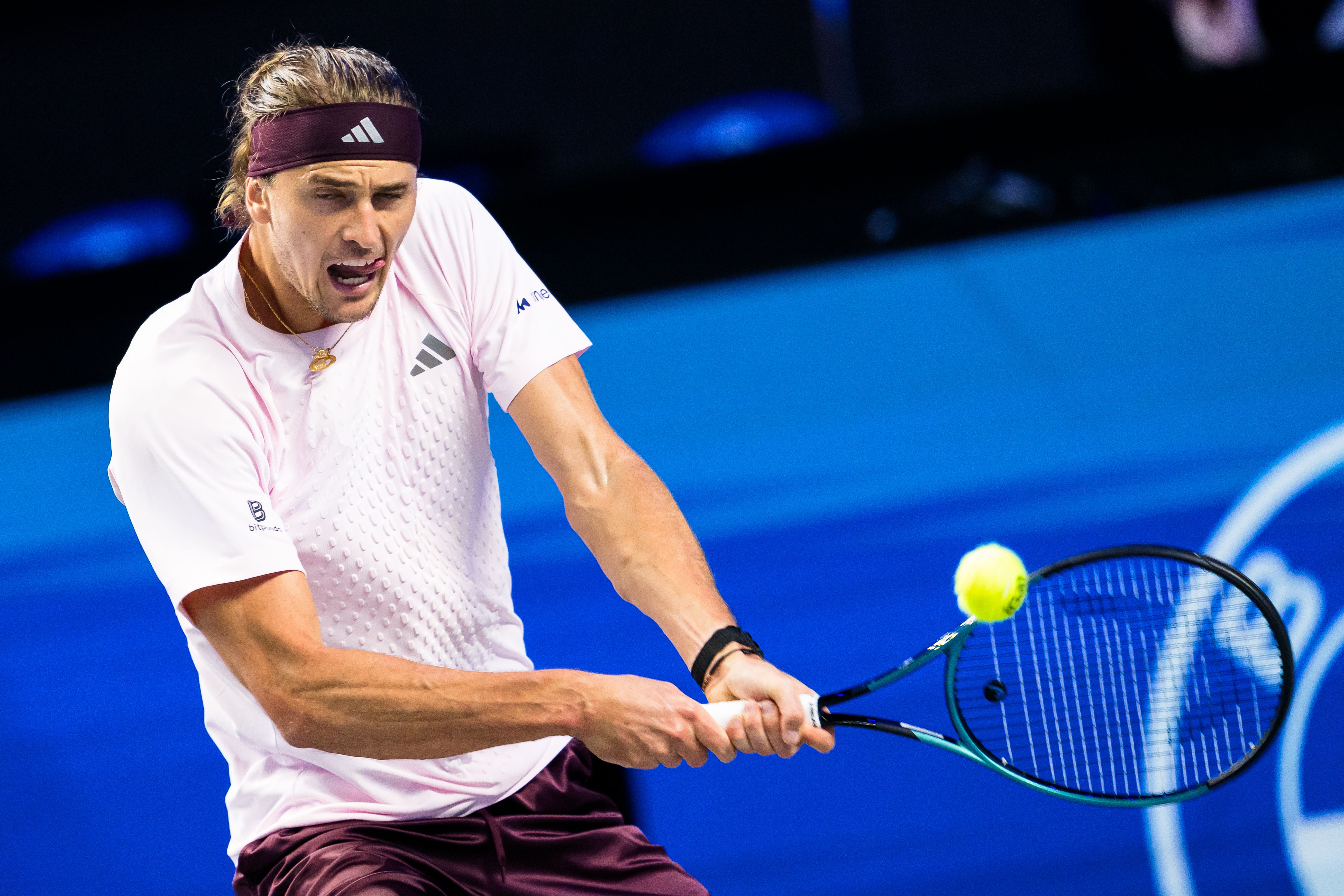 Tennisspieler schlägt einen Ball während eines Spiels auf blauem Tennisplatz.