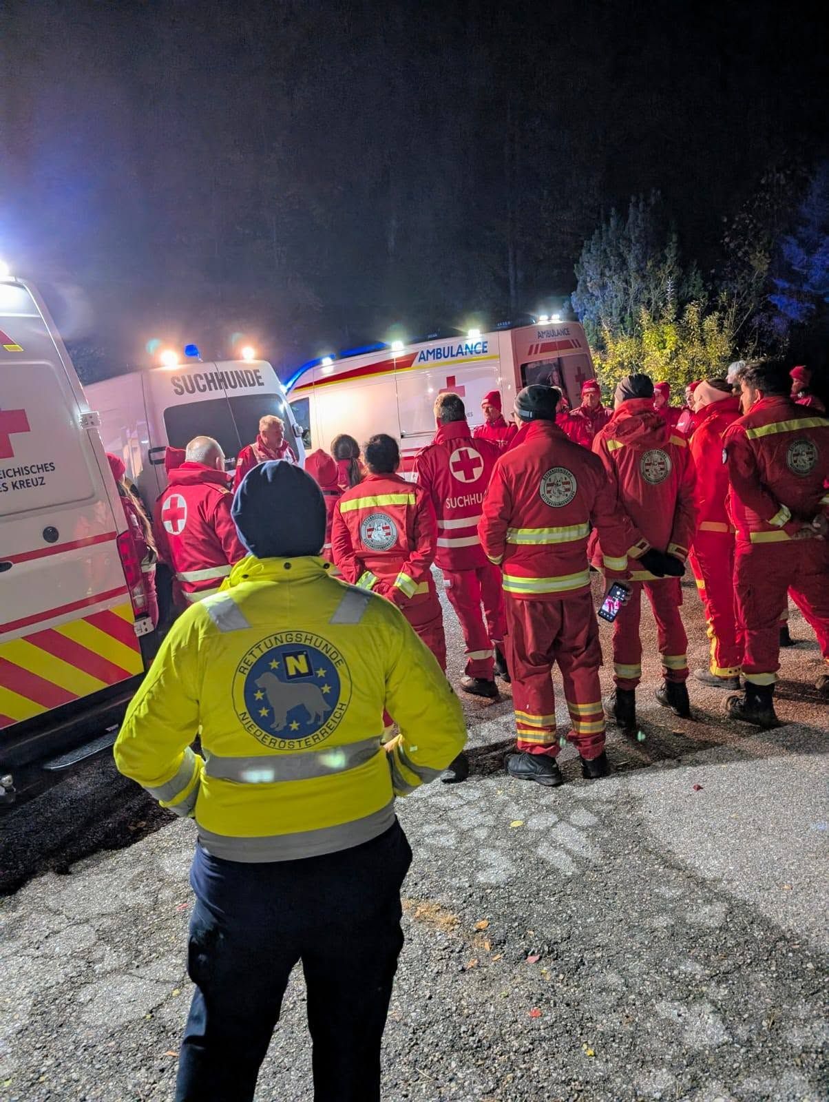 Mehrere Einsatzkräfte in reflektierender Einsatzkleidung stehen bei Einsatzfahrzeugen in der Nacht.