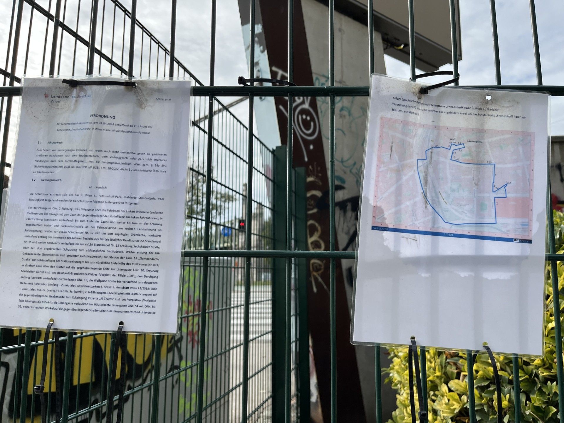 Zwei Dokumente an einem Zaun, eines mit Text, das andere zeigt eine Karte eines markierten Bereichs.