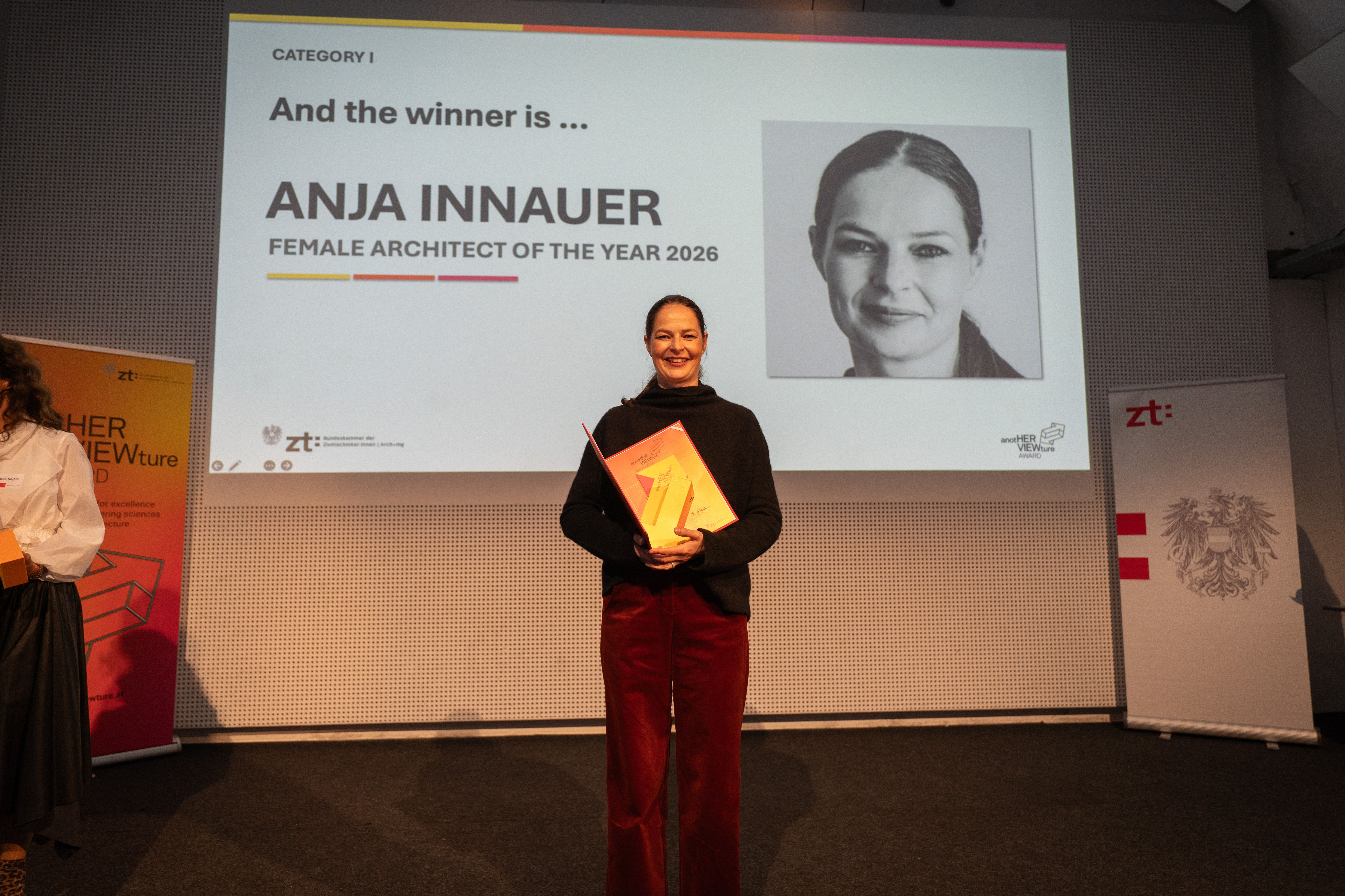 Frau hält Trophäe vor Leinwand mit Text "And the winner is ... ANJA INNAUER FEMALE ARCHITECT OF THE YEAR 2026".