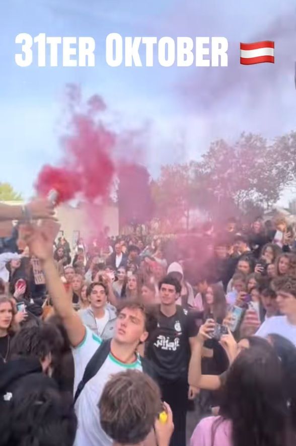 Viele Jugendliche feiern draußen mit Rauchfackeln, darüber steht „31ter Oktober“ und eine Österreich-Flagge.