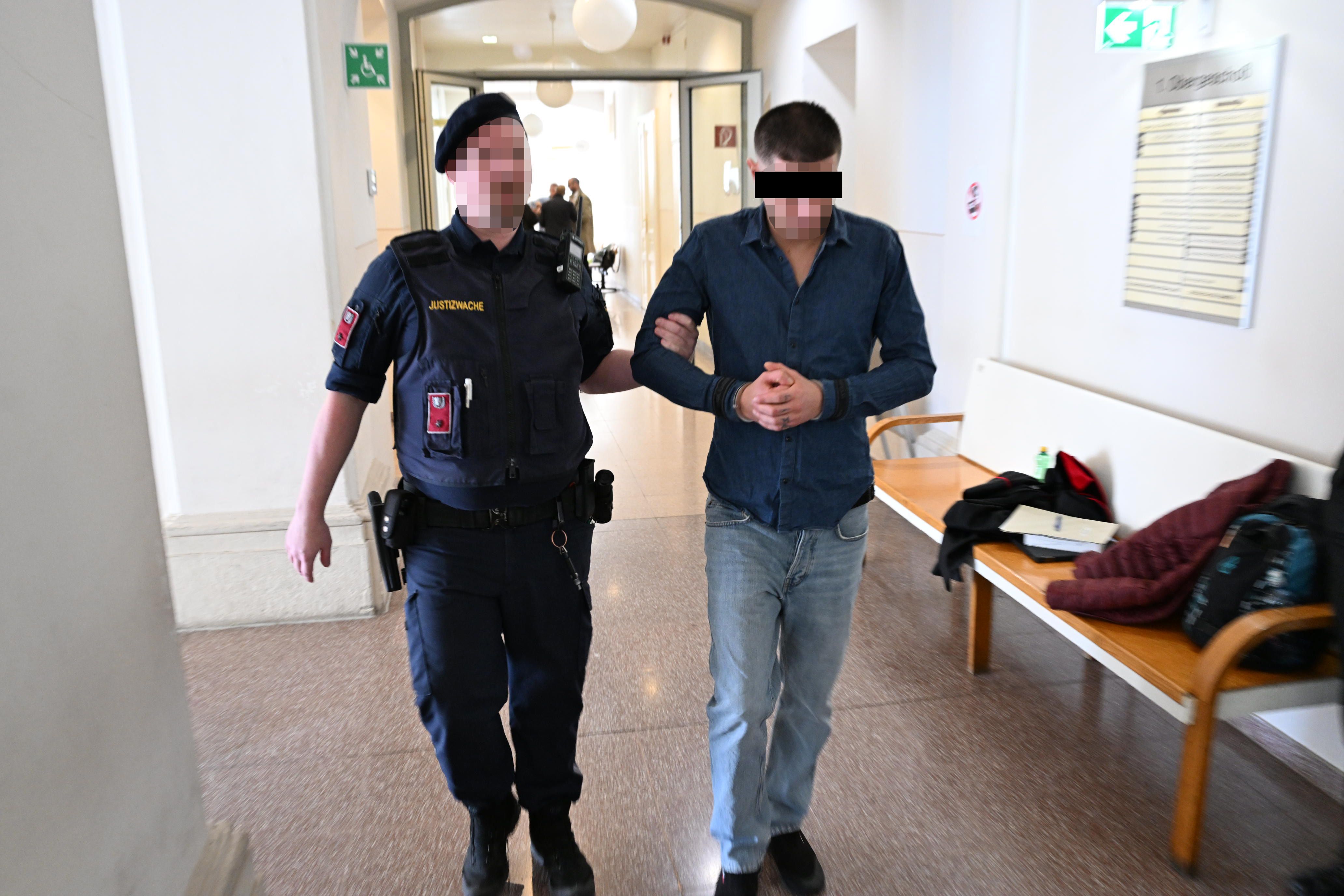Ein Polizist führt einen angeklagten Mann mit Handschellen durch einen Gerichtsflur.