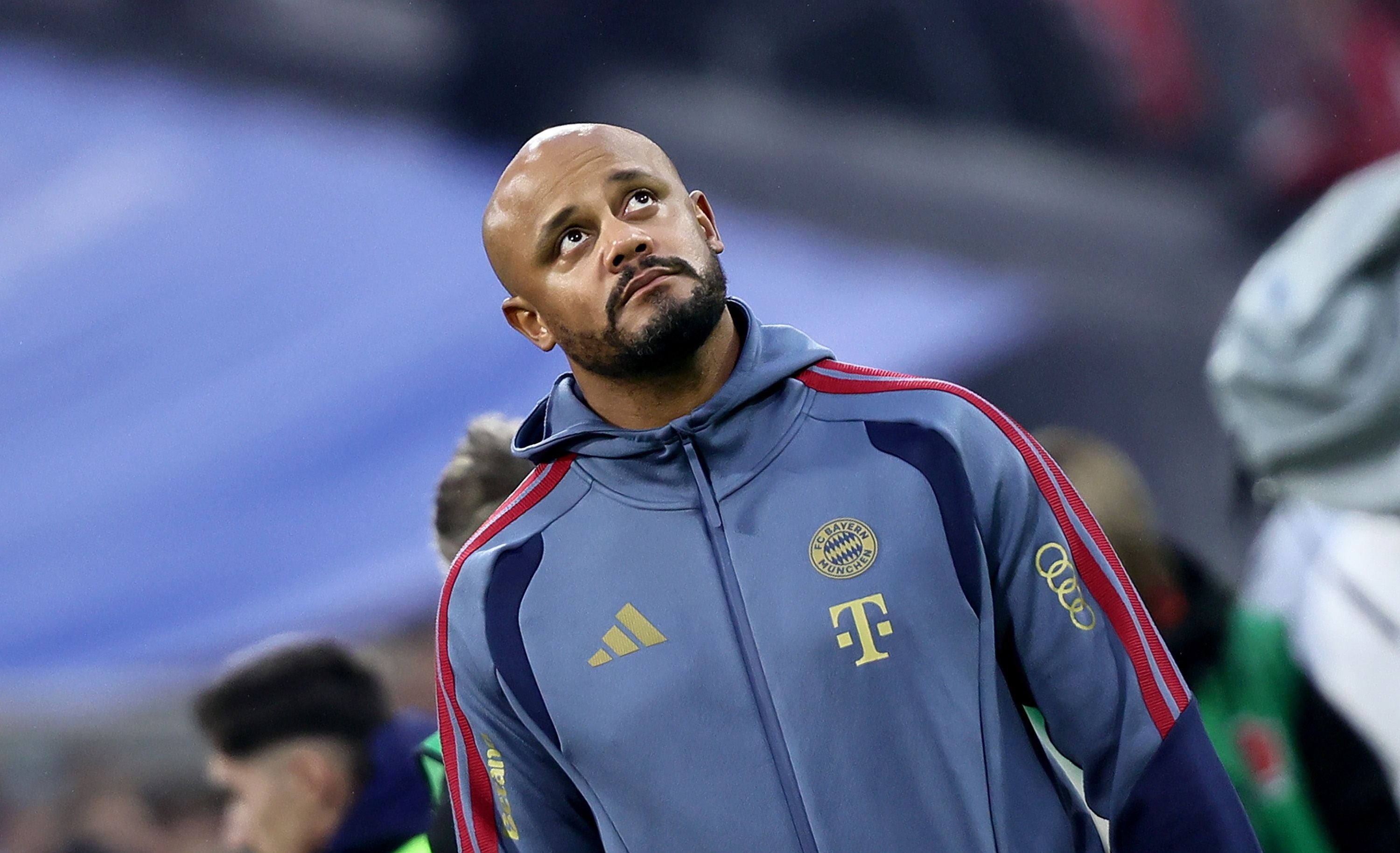 Ein Fußballtrainer im Bayern-München-Trainingsanzug blickt nachdenklich nach oben.