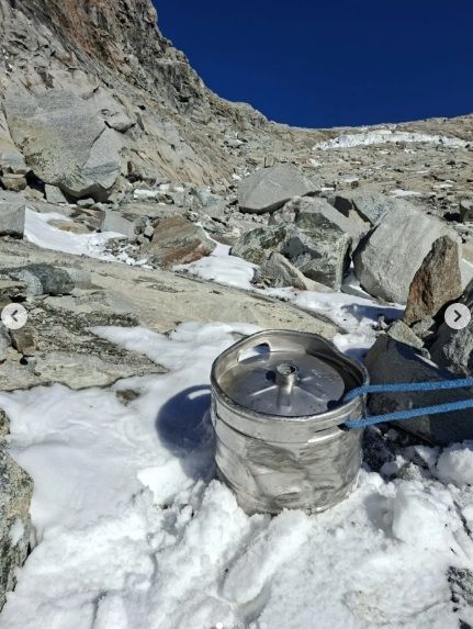 Ein Bierfass steht im verschneiten, felsigen Gebirge unter blauem Himmel.