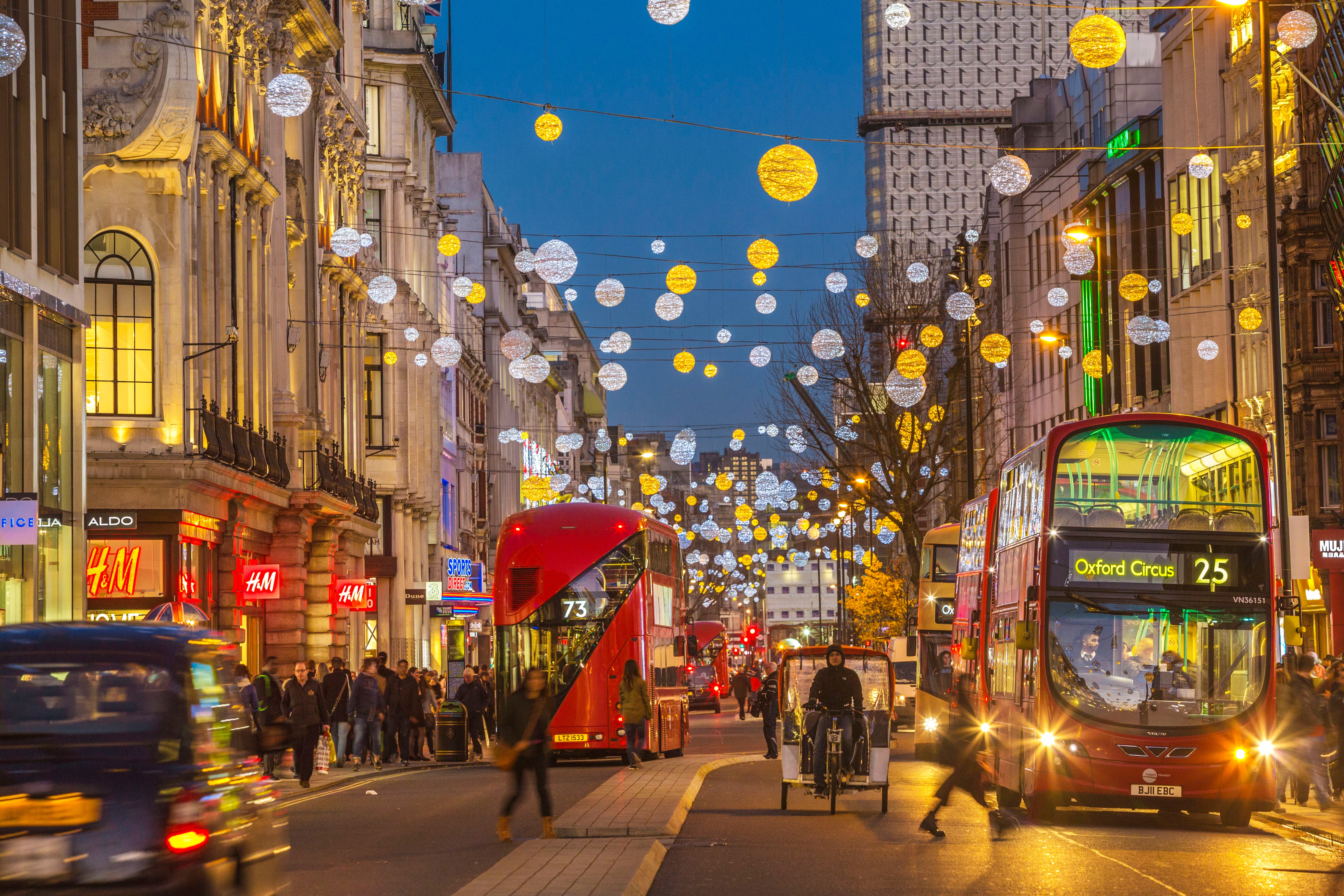 Abendliche Oxford Street in London mit festlicher Beleuchtung und roten Doppeldeckerbussen.