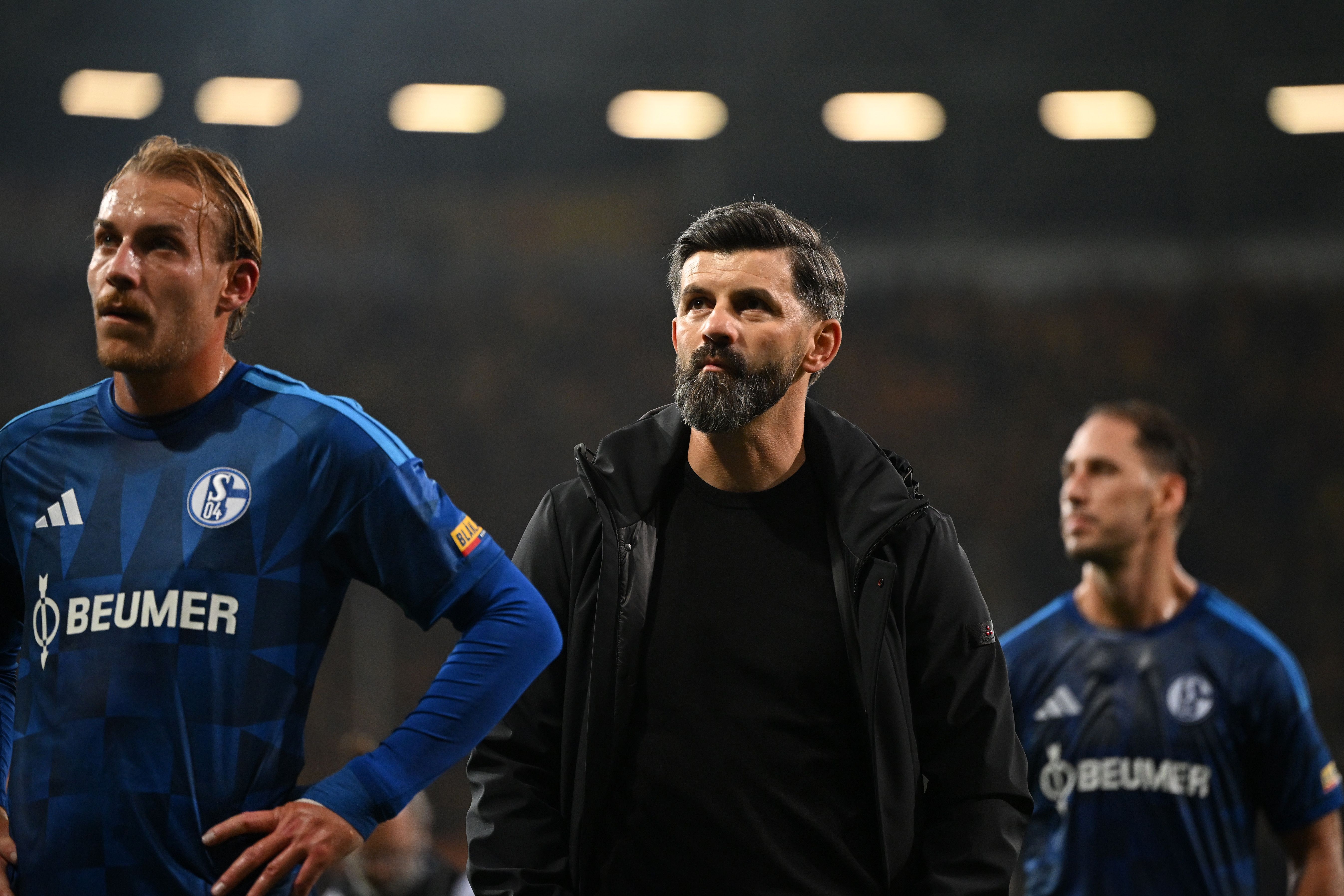 Drei enttäuschte Schalke-Spieler und ihr Trainer nach einer Niederlage im Fußballstadion.