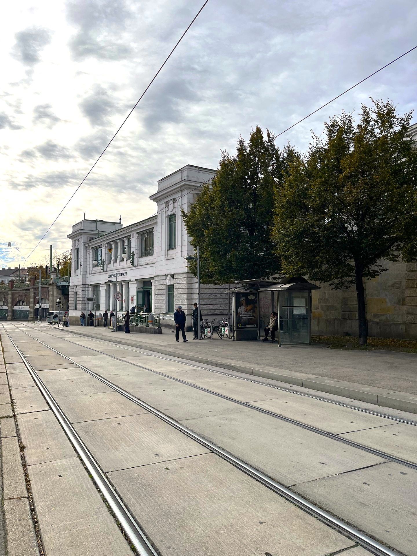 Straßenbahngleise, eine Haltestelle und das Gebäude der U6 Gumpendorfer Straße bei bewölktem Himmel.