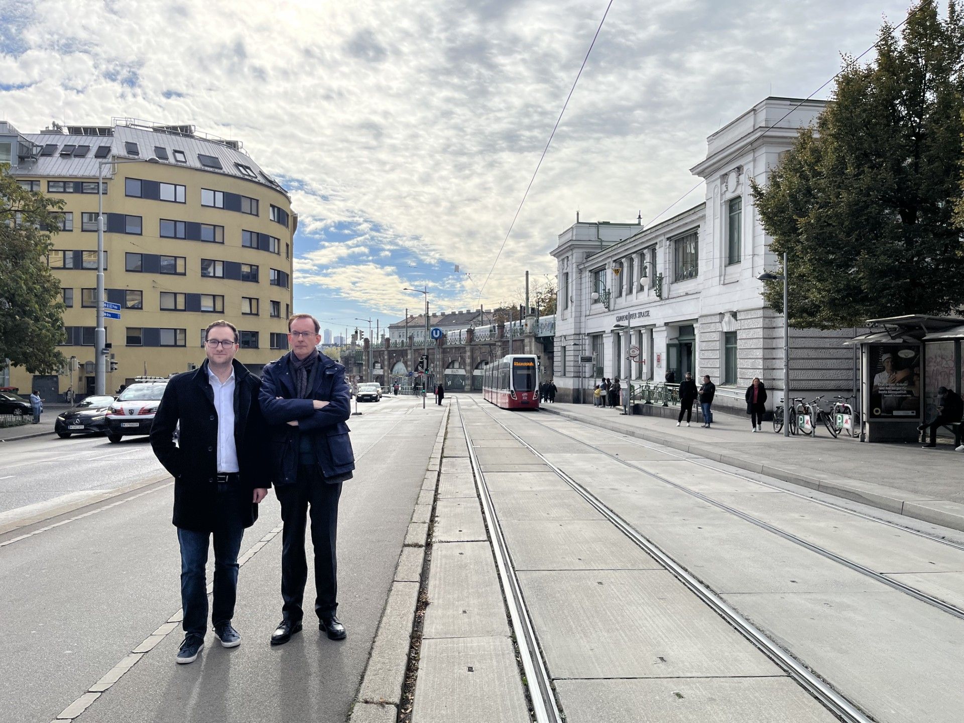 Zwei Männer stehen auf einer Straße neben Straßenbahngleisen bei der U6 Gumpendorfer Straße.