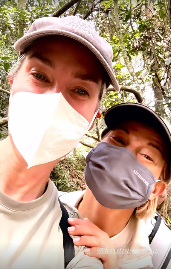 Zwei Frauen mit Masken und Kappen im Wald während eines Gorilla-Trekkings.