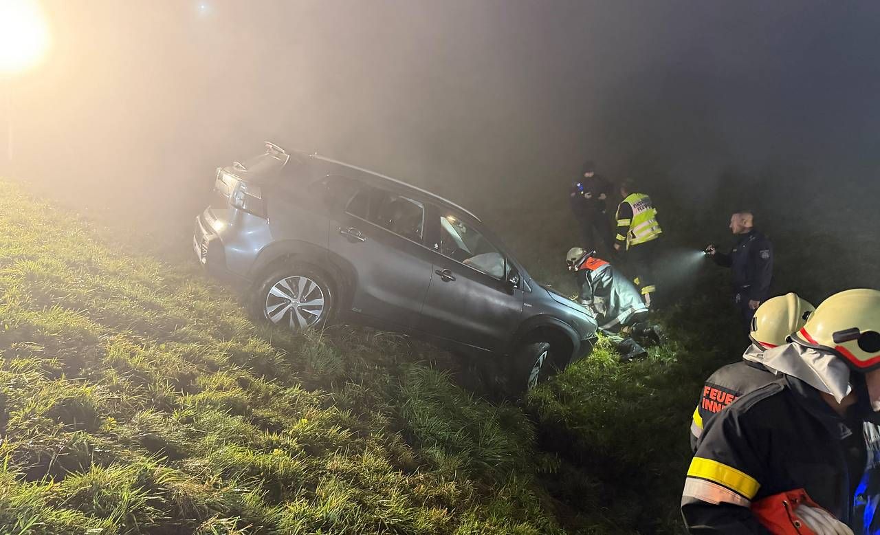 Feuerwehr und Polizei helfen bei einem verunglückten Auto auf einer nassen, nebligen Wiese.