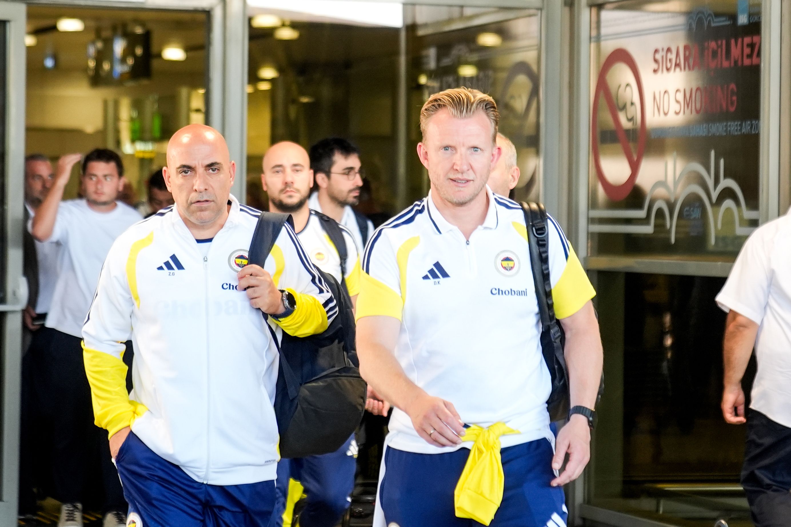Dirk Kuyt geht gemeinsam mit einem Betreuer in Trainingskleidung von Fenerbahçe Istanbul durch einen Flughafenausgang.