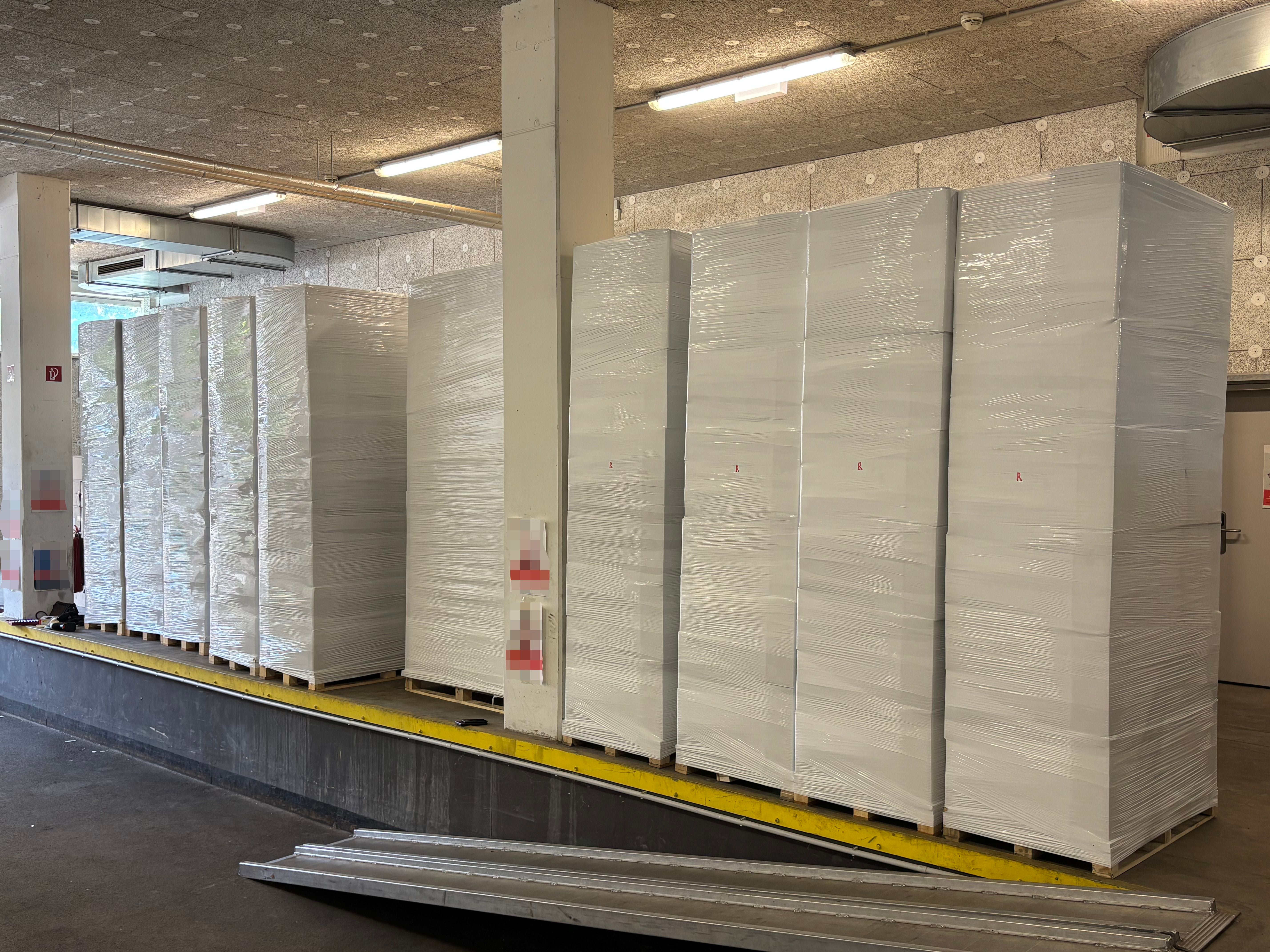 Mehrere große, in Folie verpackte Paletten stehen in einer Lagerhalle auf einer Rampe.