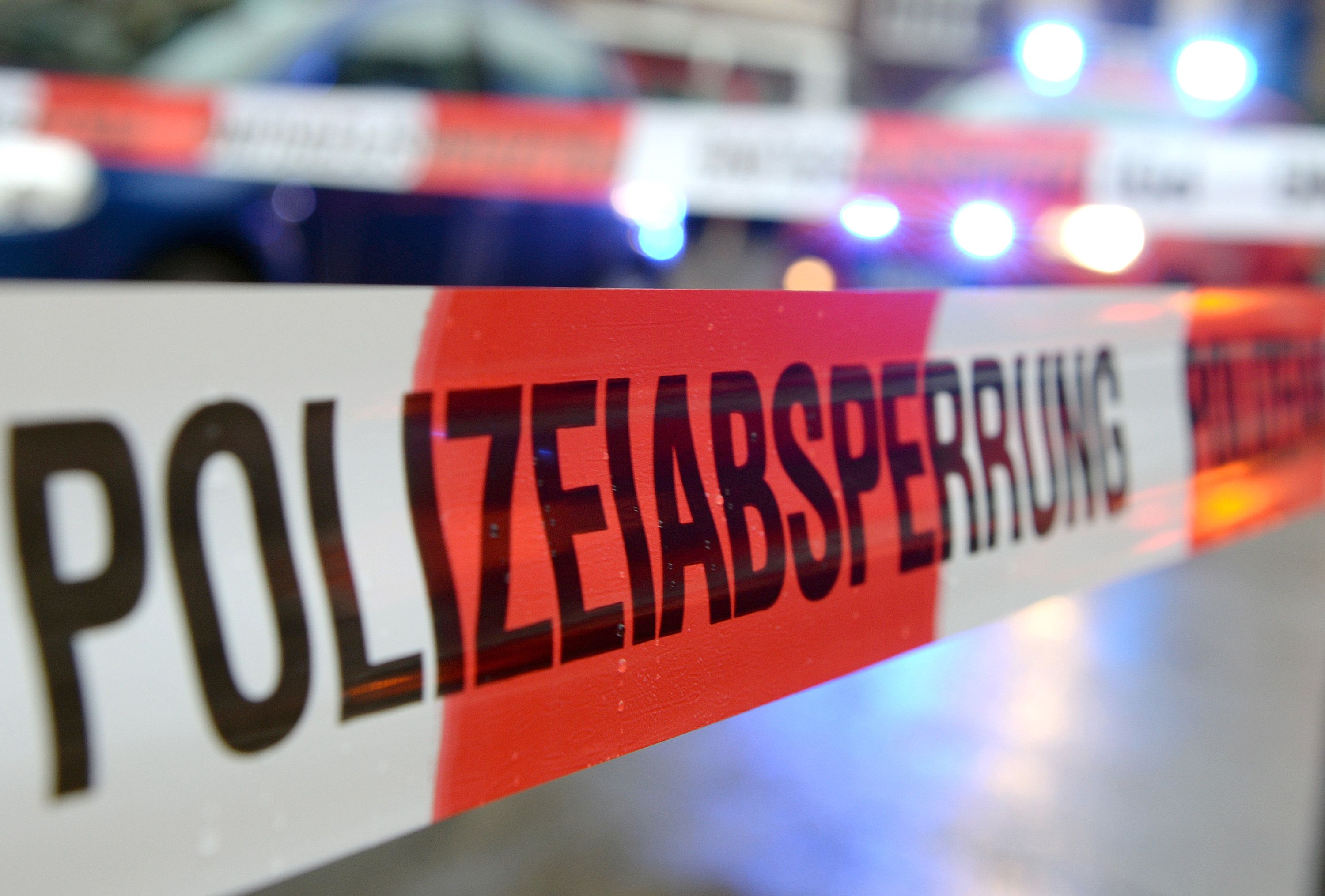 Ein Polizeiabsperrband vor einem Einsatzfahrzeug mit eingeschaltetem Blaulicht.