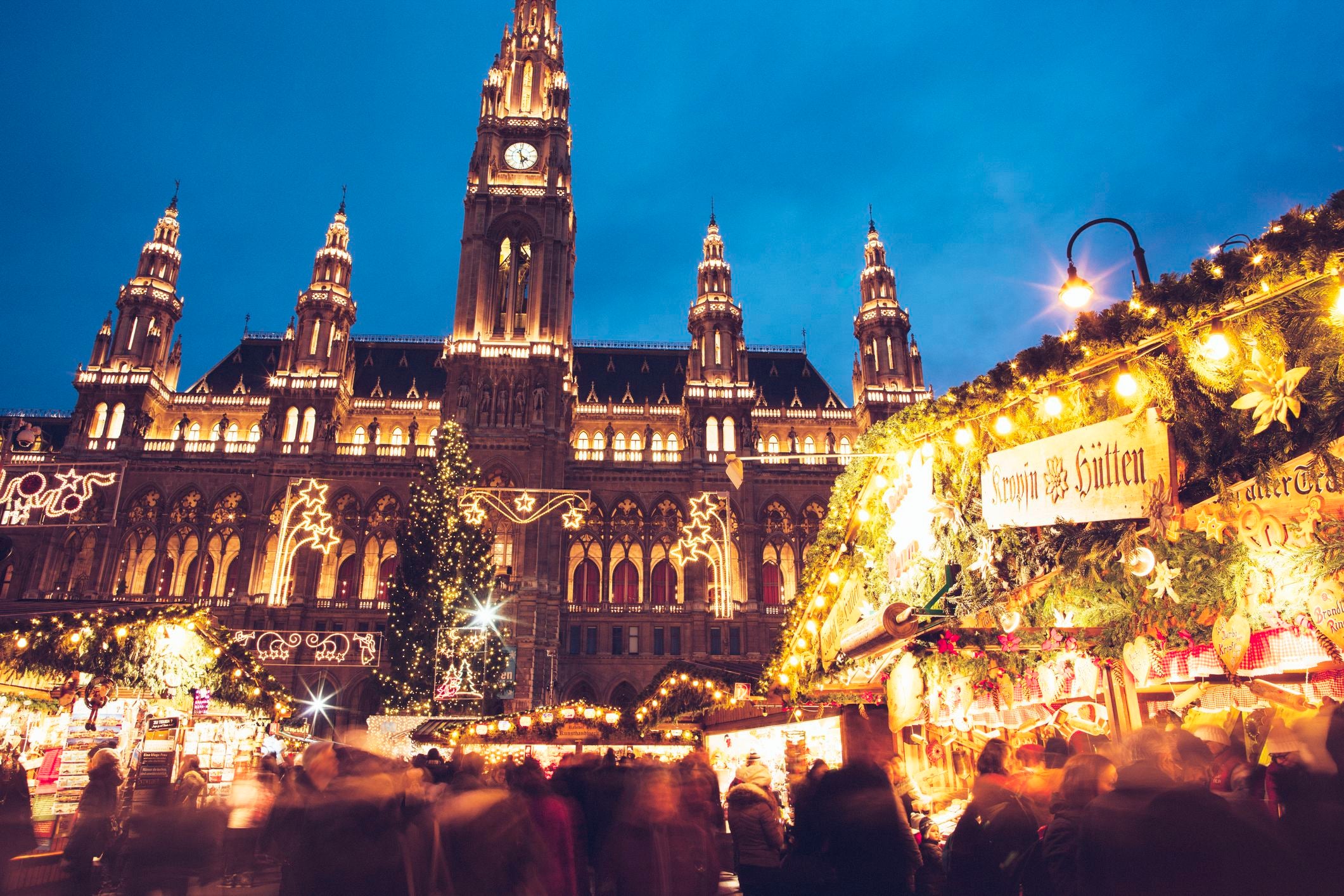 Belebter Weihnachtsmarkt mit festlicher Beleuchtung vor dem Wiener Rathaus am Abend.