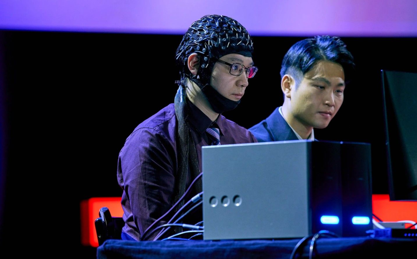 Zwei Männer sitzen bei einem TED-Talk an Computern, einer trägt ein EEG-Haarnetz.