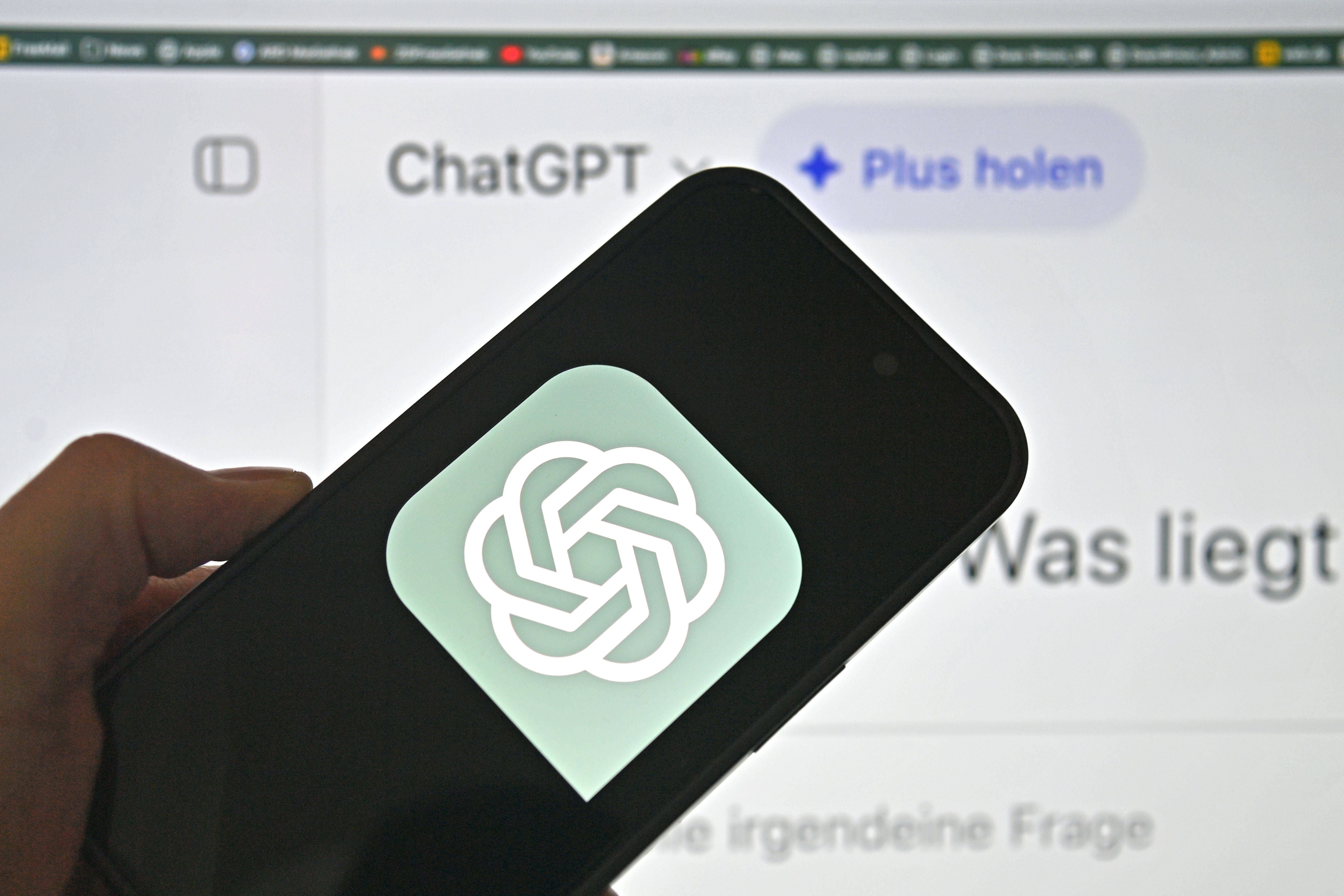 Ein Smartphone zeigt das ChatGPT-Logo vor einem ChatGPT-Bildschirm im Hintergrund.