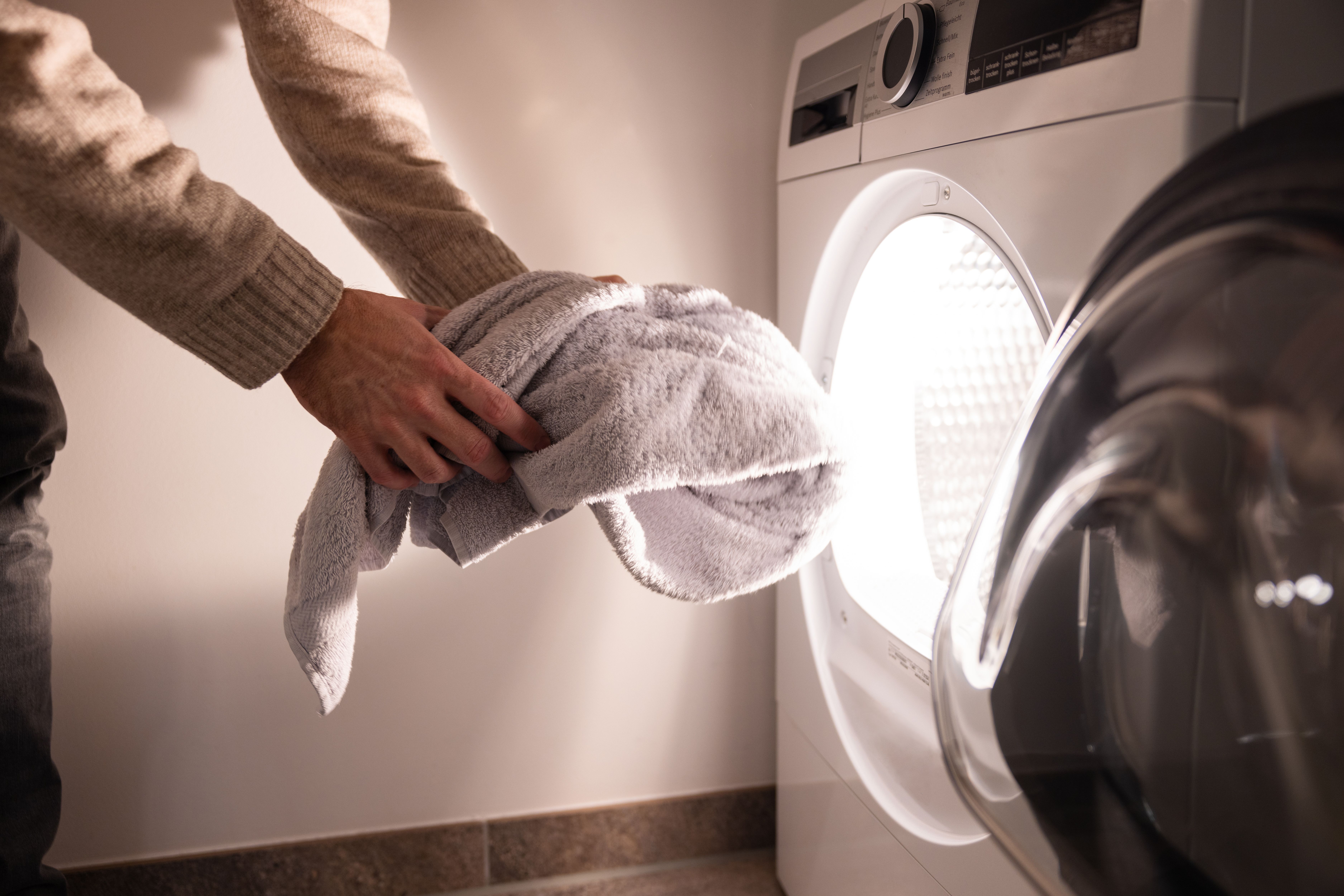 Person legt ein Handtuch in eine geöffnete Waschmaschine.