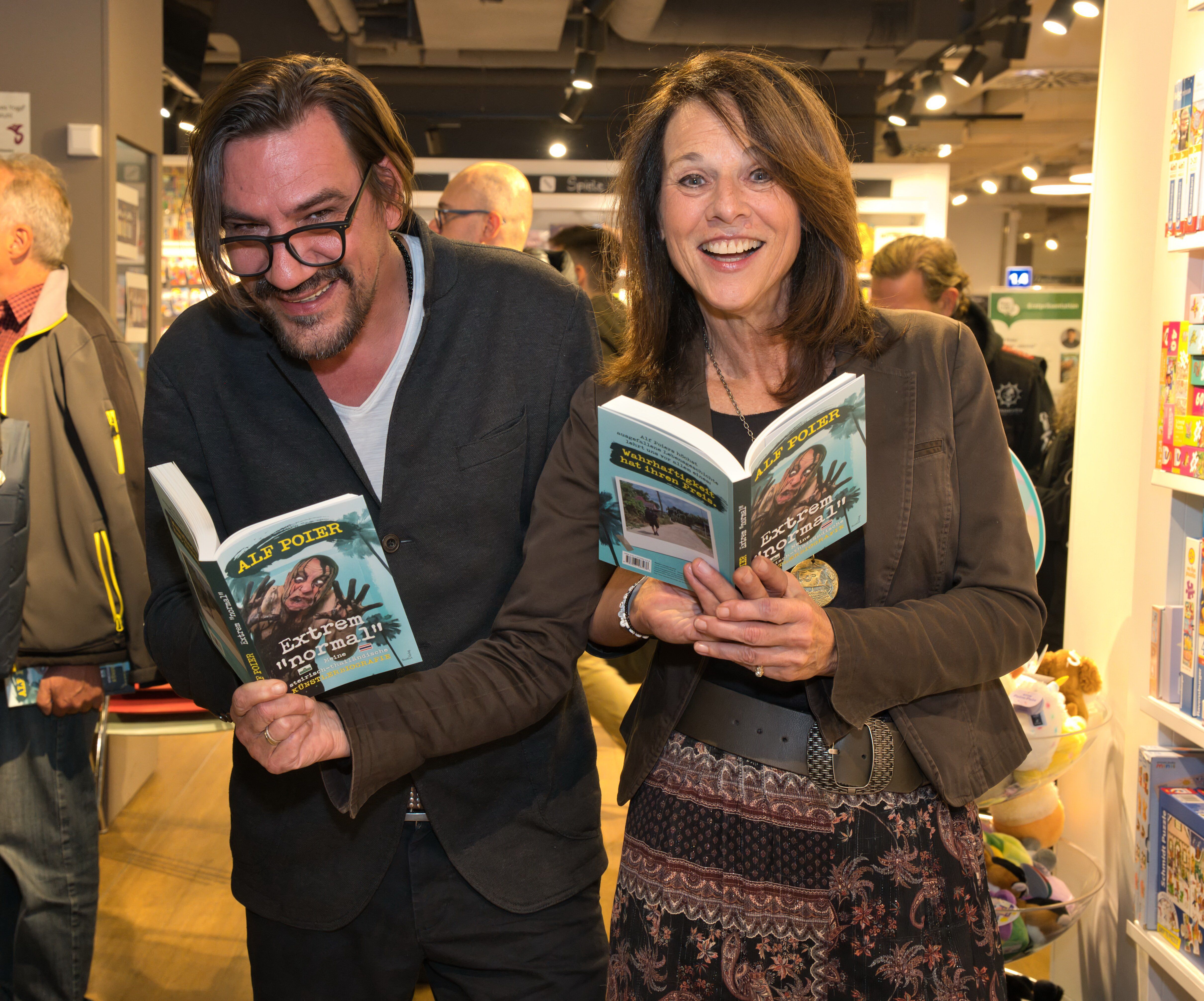 Zwei lachende Personen halten das Buch "Extrem normal!" bei einer Buchpräsentation in der Hand.