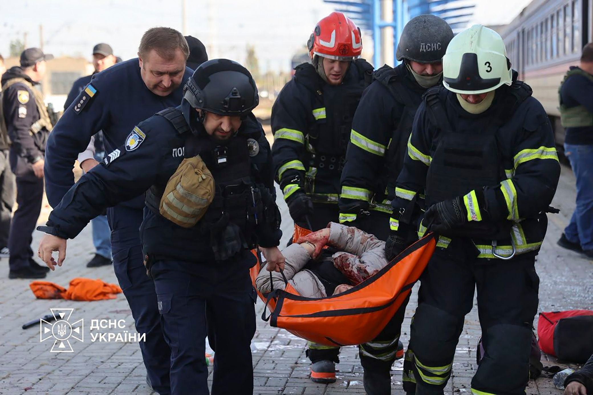 Ukrainische Rettungskräfte tragen eine verletzte Person auf einer Trage an einem Bahnhof.