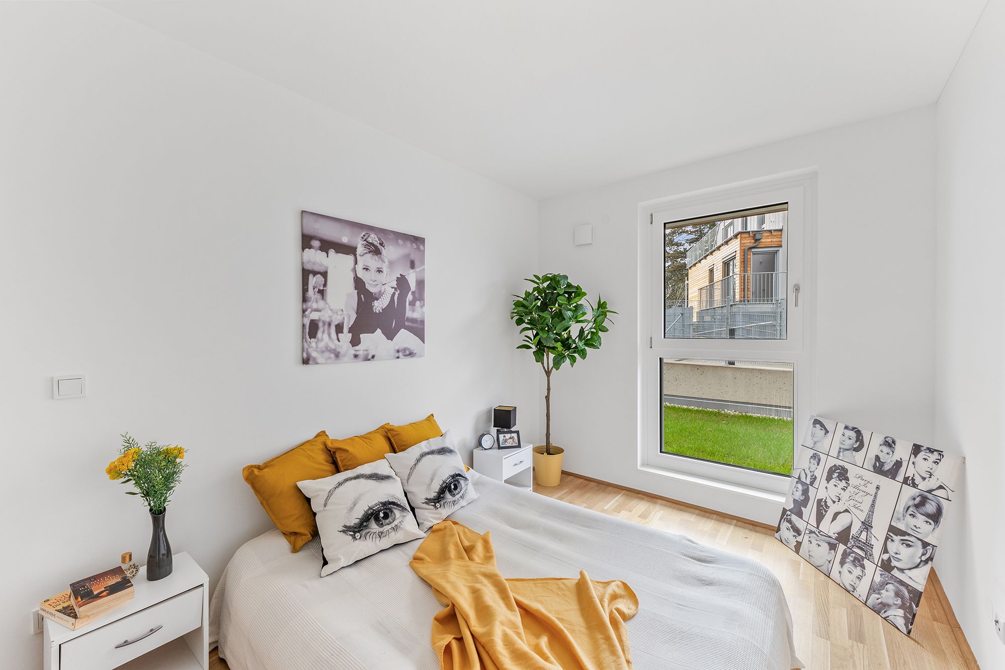 Helles Schlafzimmer mit gelbem Akzent, großem Fenster und Audrey Hepburn-Bildern an den Wänden.
