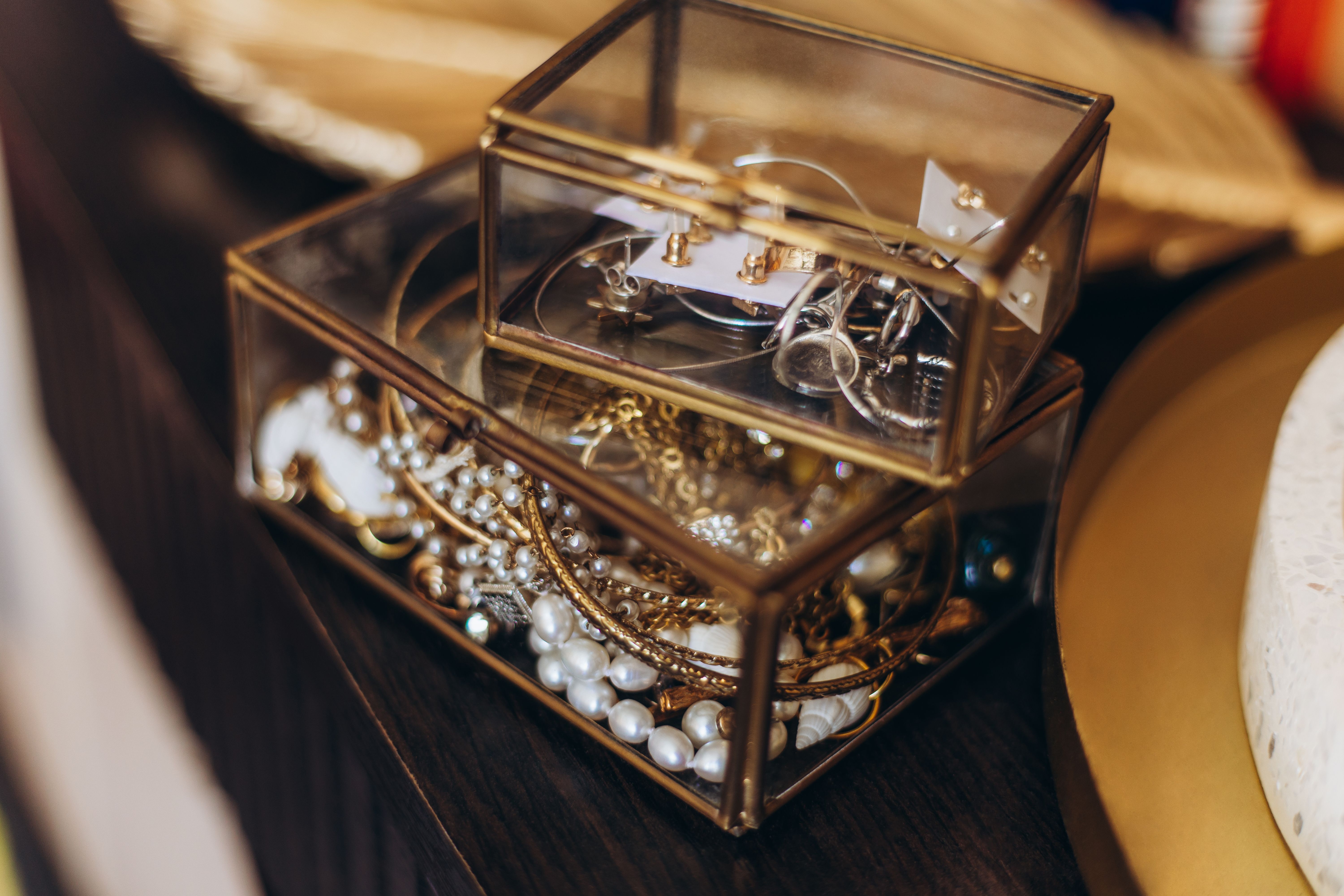Schmuck in zwei Glasboxen, umgeben von goldenem Tablett auf dunklem Tisch.