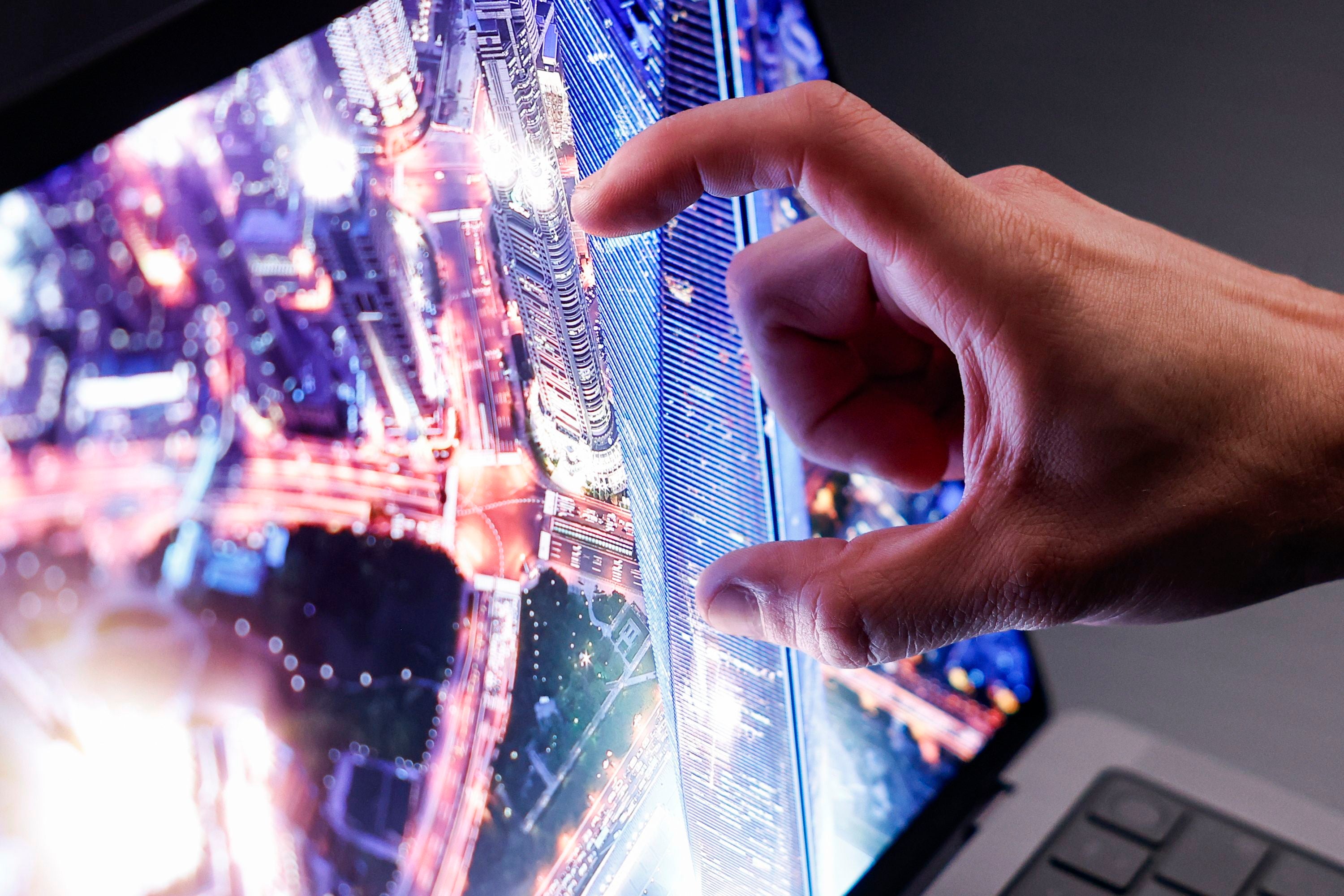 Eine Hand nutzt die Zoom-Geste auf einem Laptop mit Luftbild einer beleuchteten Stadt.