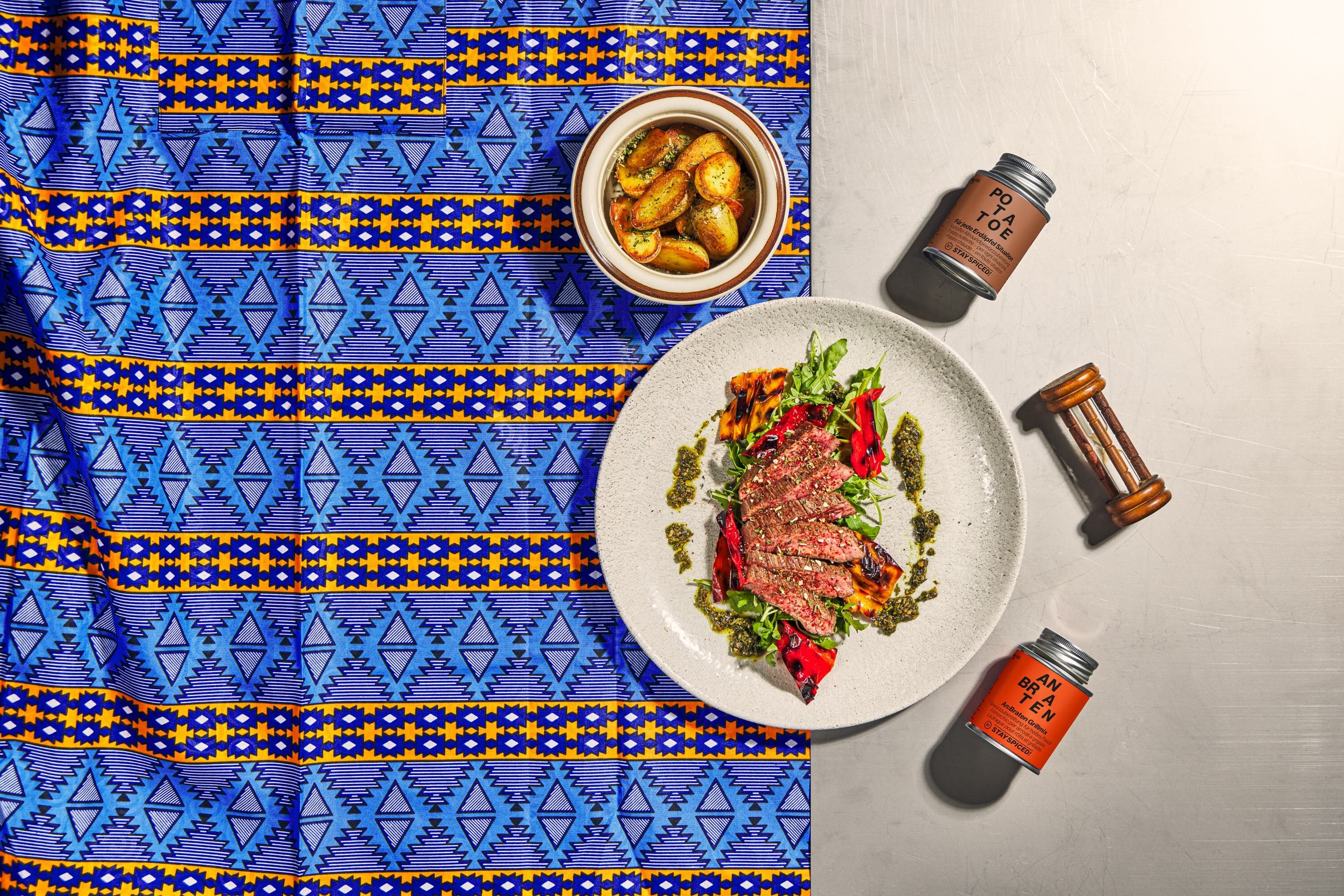 Ein Teller mit Steak, Gemüse und Kräutern, daneben Bratkartoffeln und zwei Gewürzdosen.