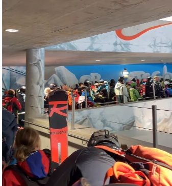 Viele Skifahrer mit Ausrüstung stehen in einer Schlange in einem Gletschergebäude.