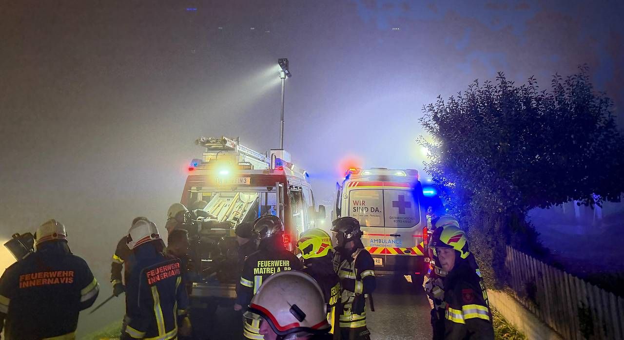 Mehrere Feuerwehrleute und Rettungswagen bei einem nächtlichen Unfall mit starker Rauchentwicklung.