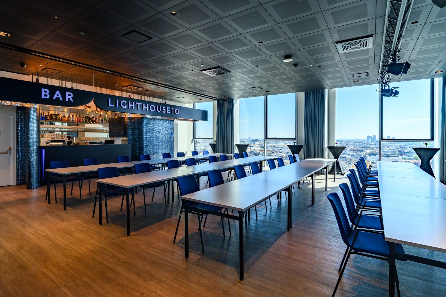 Moderner Tagungsraum mit blauen Stühlen, Bar und großen Fenstern mit Blick über die Stadt.