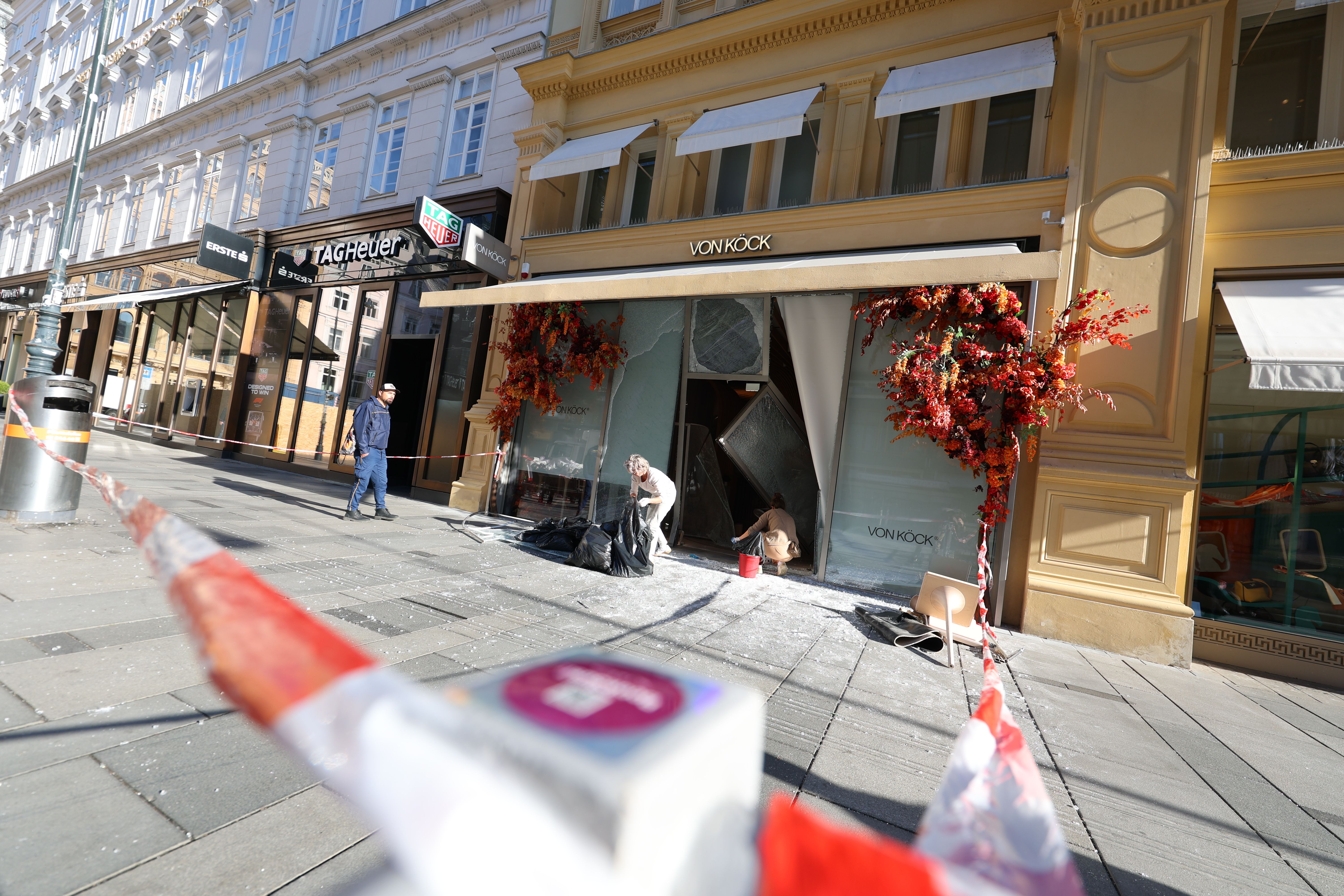 Aufräumarbeiten vor einem Juwelier mit zerstörter Schaufensterfront in Wien, Absperrband im Vordergrund.