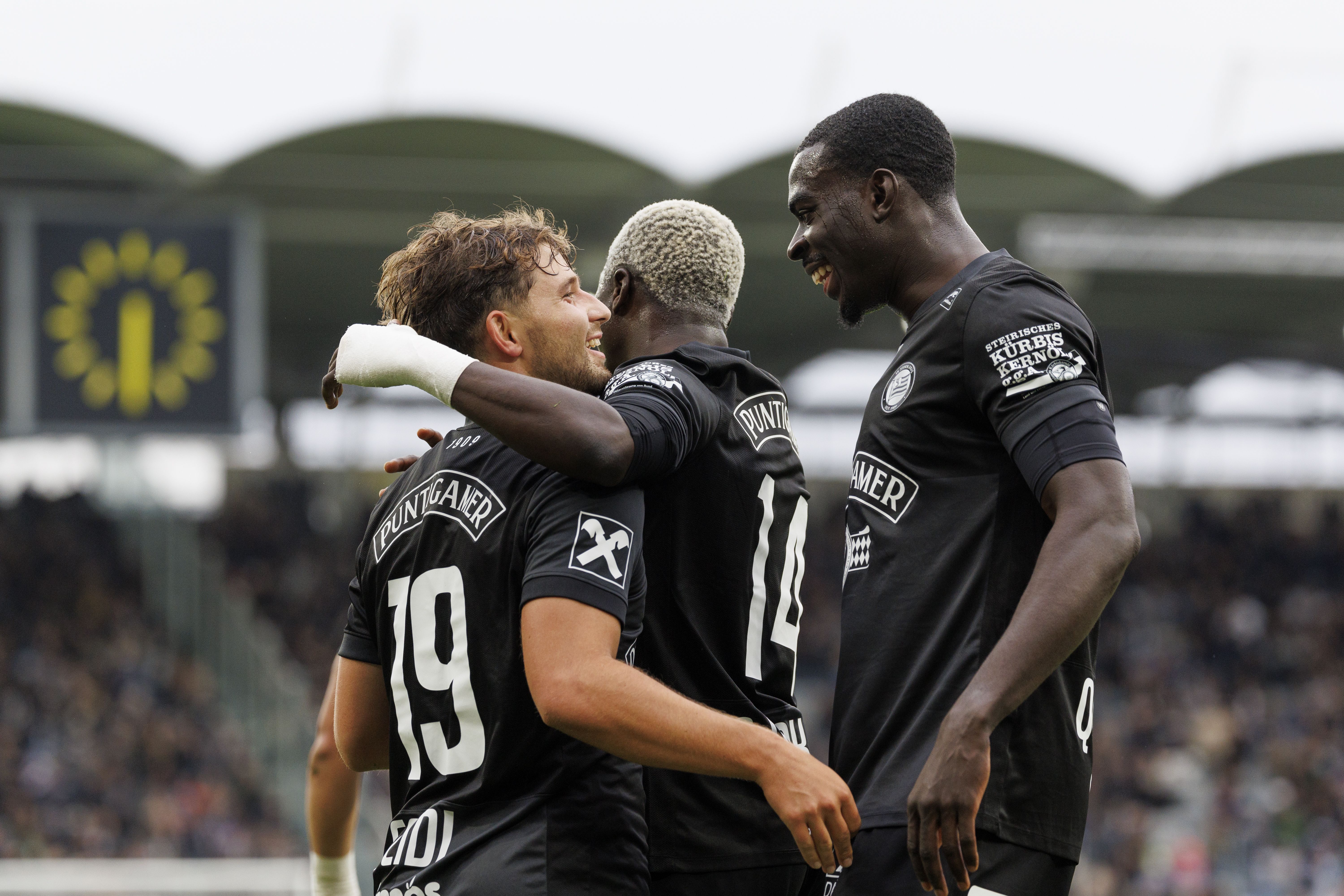 Belmin Beganovic jubelt im schwarzen Trikot des SK Sturm Graz gemeinsam mit zwei Teamkollegen auf dem Spielfeld.