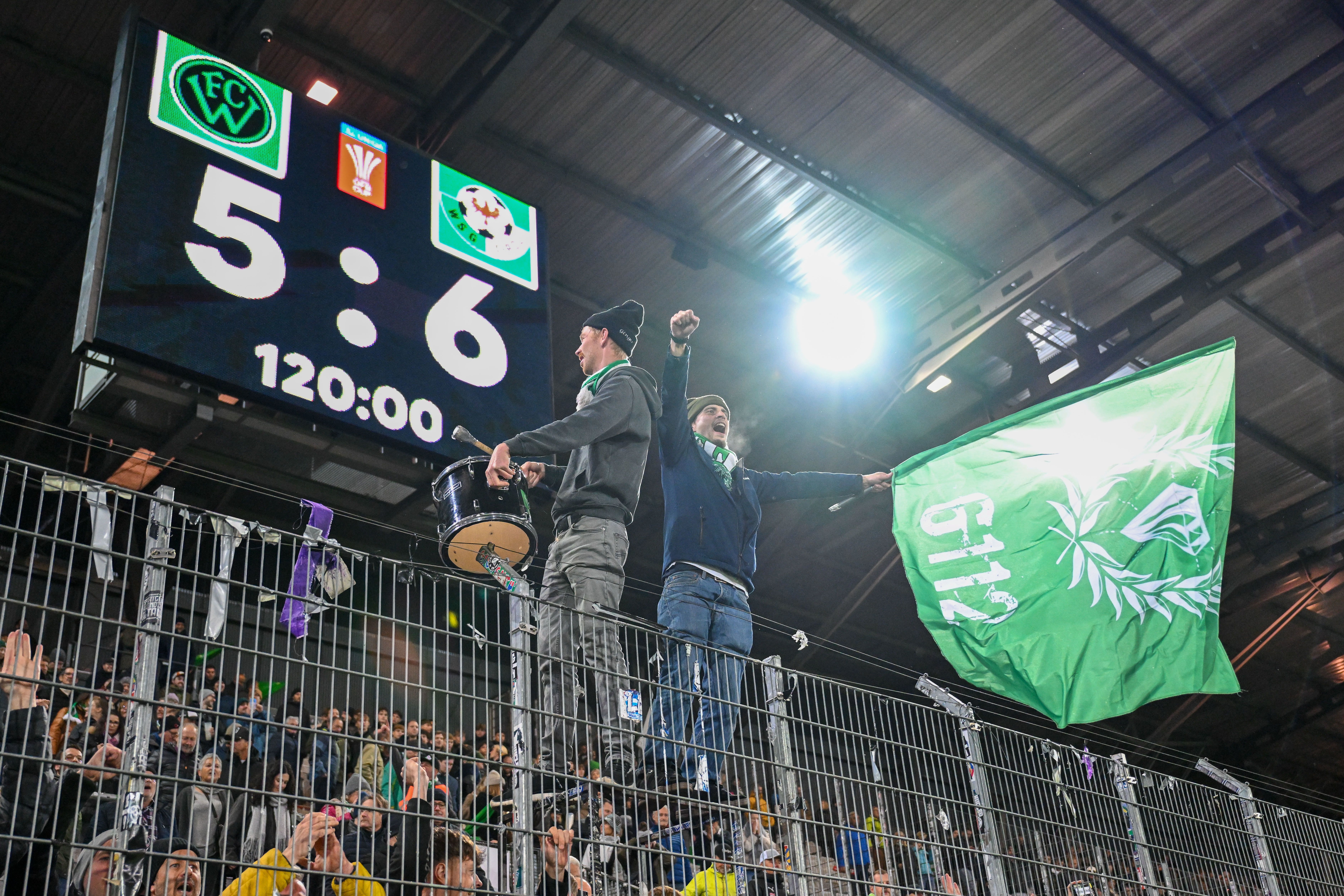 Fans feiern vor einer Anzeigetafel mit dem Endstand 5:6 nach Verlängerung im Fußballstadion.