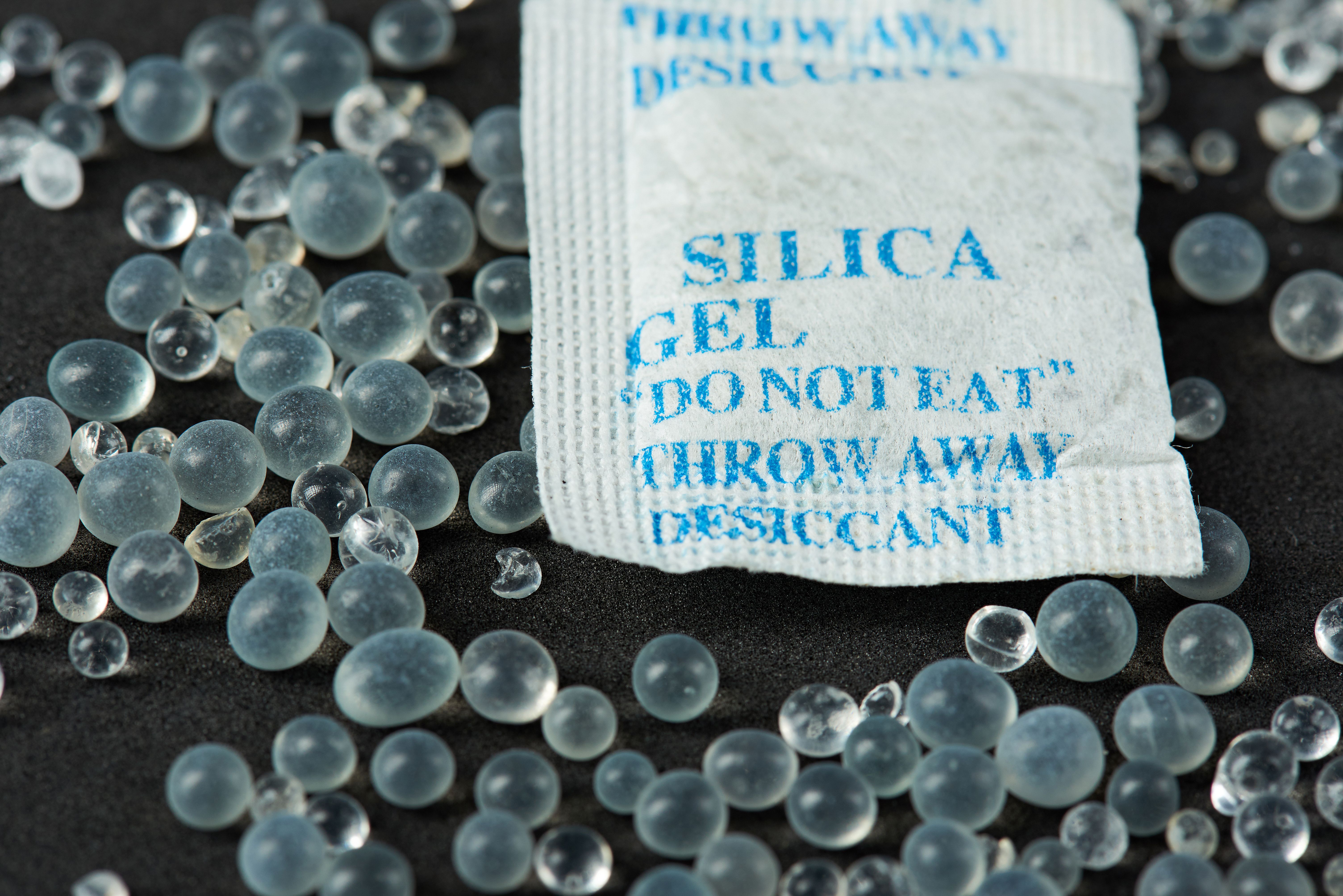 Nahaufnahme eines Silica-Gel-Beutels mit verstreuten Gel-Kügelchen auf schwarzem Hintergrund.