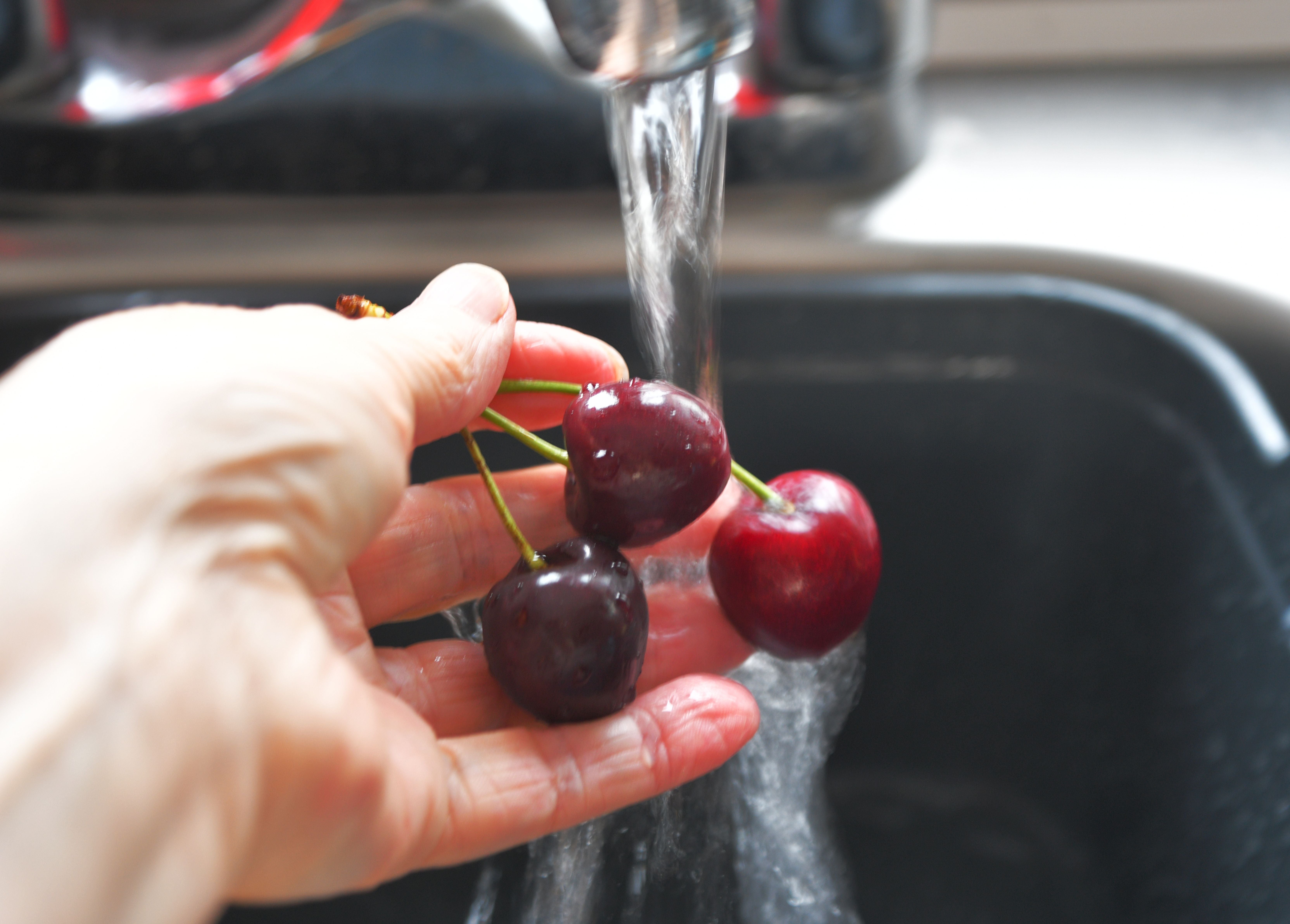 Eine Hand wäscht Kirschen unter fließendem Wasser in einer Küchenspüle.