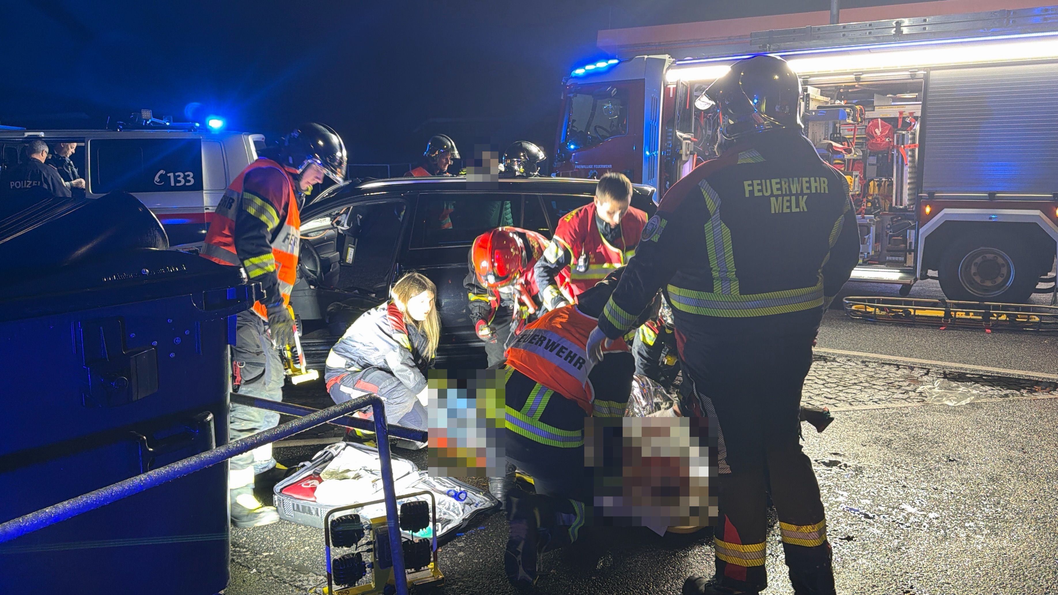 Rettungskräfte und Feuerwehr helfen nachts an einer Unfallstelle mit beschädigtem Auto.
