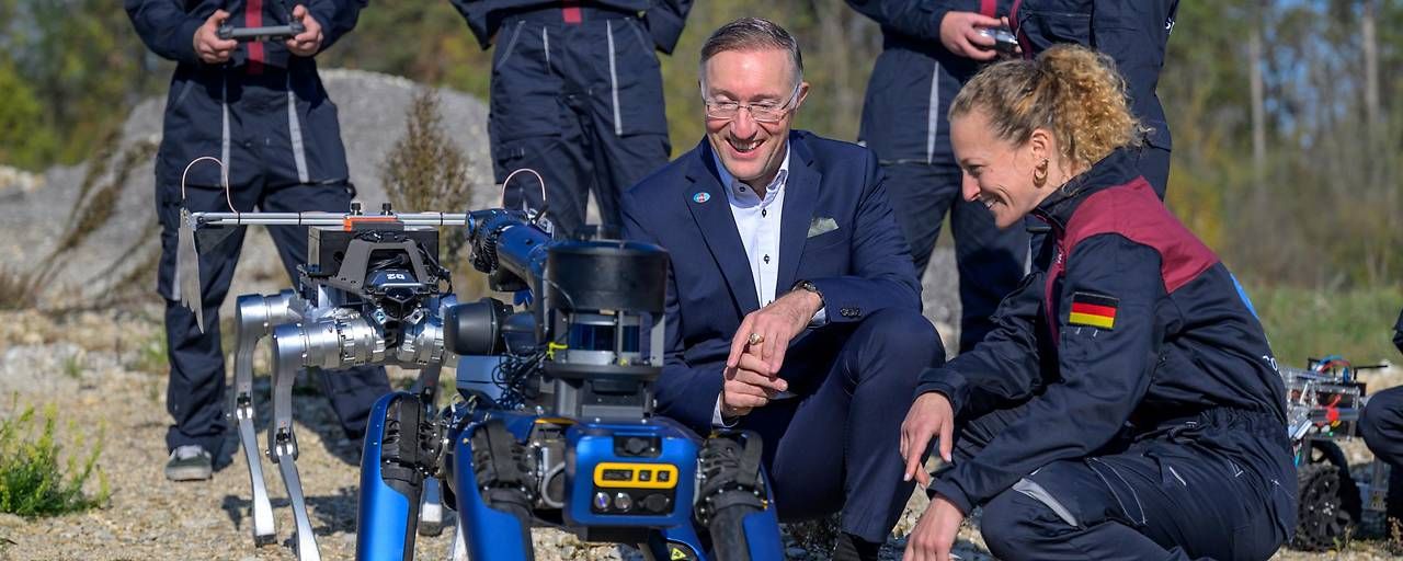 Eine Frau und ein Mann betrachten im Freien einen vierbeinigen Roboter, umgeben von Teammitgliedern.