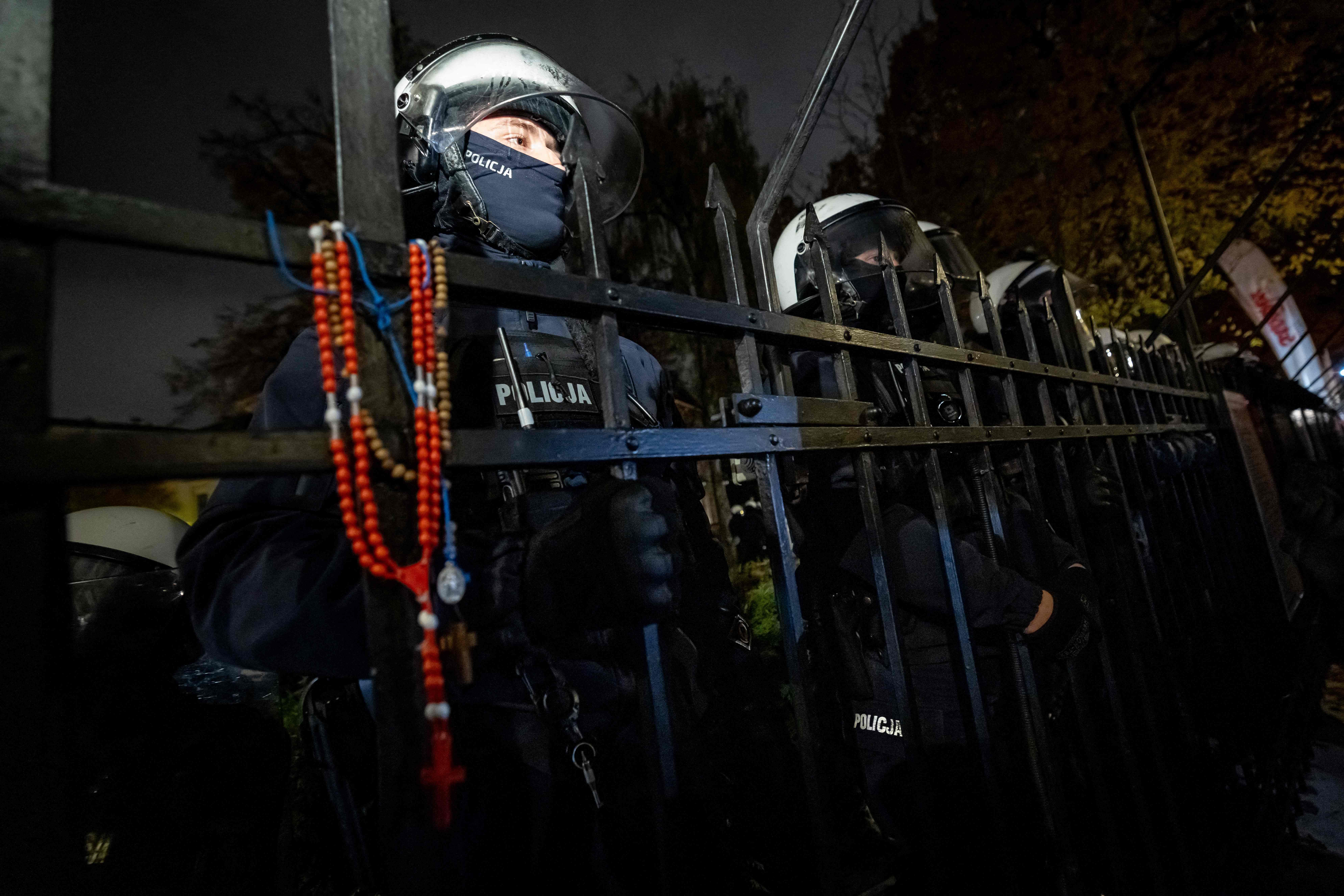 Polizisten stehen hinter einem Zaun mit Rosenkränzen, abends vor dem Verfassungsgericht in Warschau.