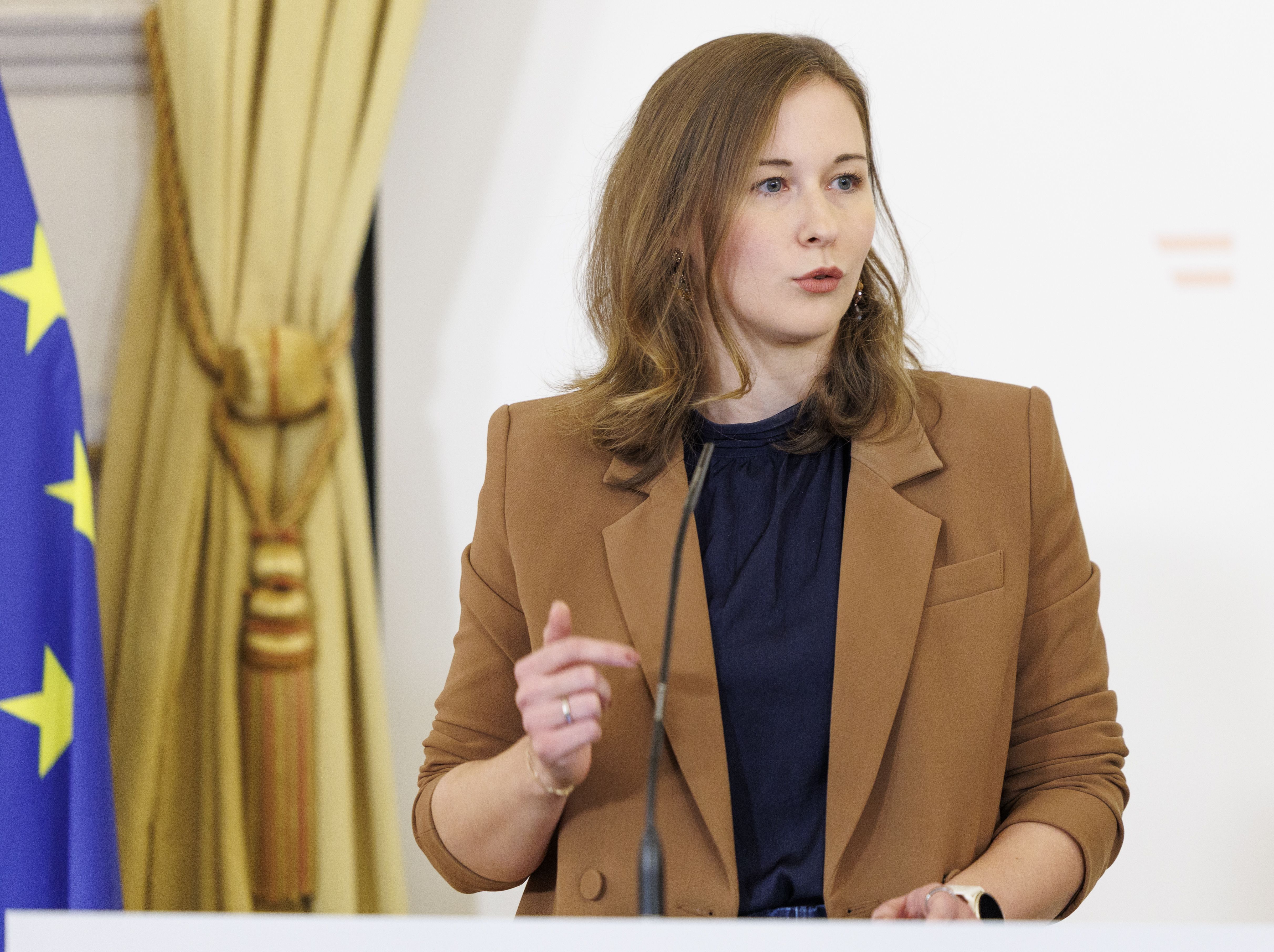 Eine Frau spricht bei einer Pressekonferenz, neben ihr ist eine EU-Flagge zu sehen.