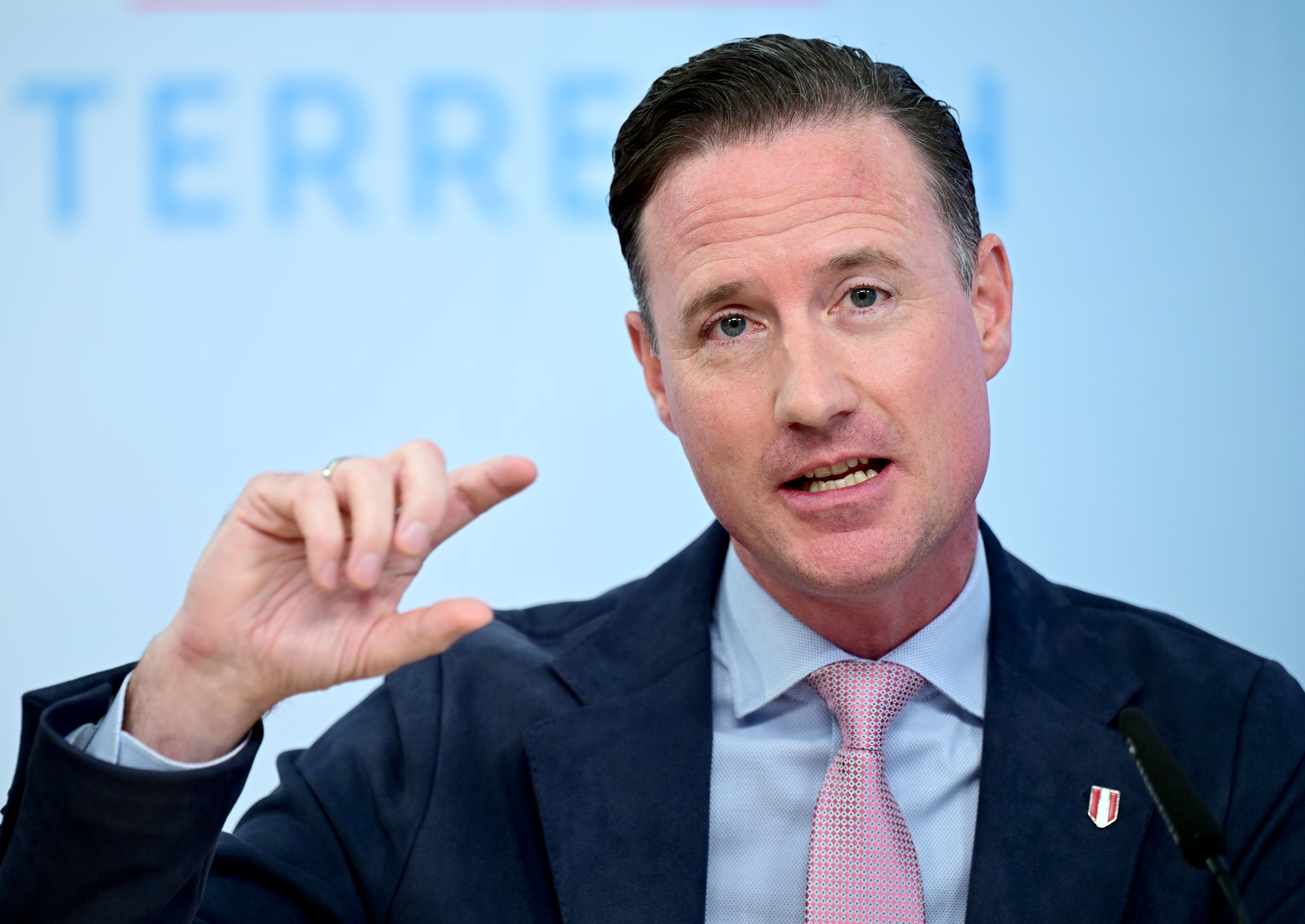 Ein Mann in Anzug und Krawatte spricht bei einer Pressekonferenz und gestikuliert mit der Hand.