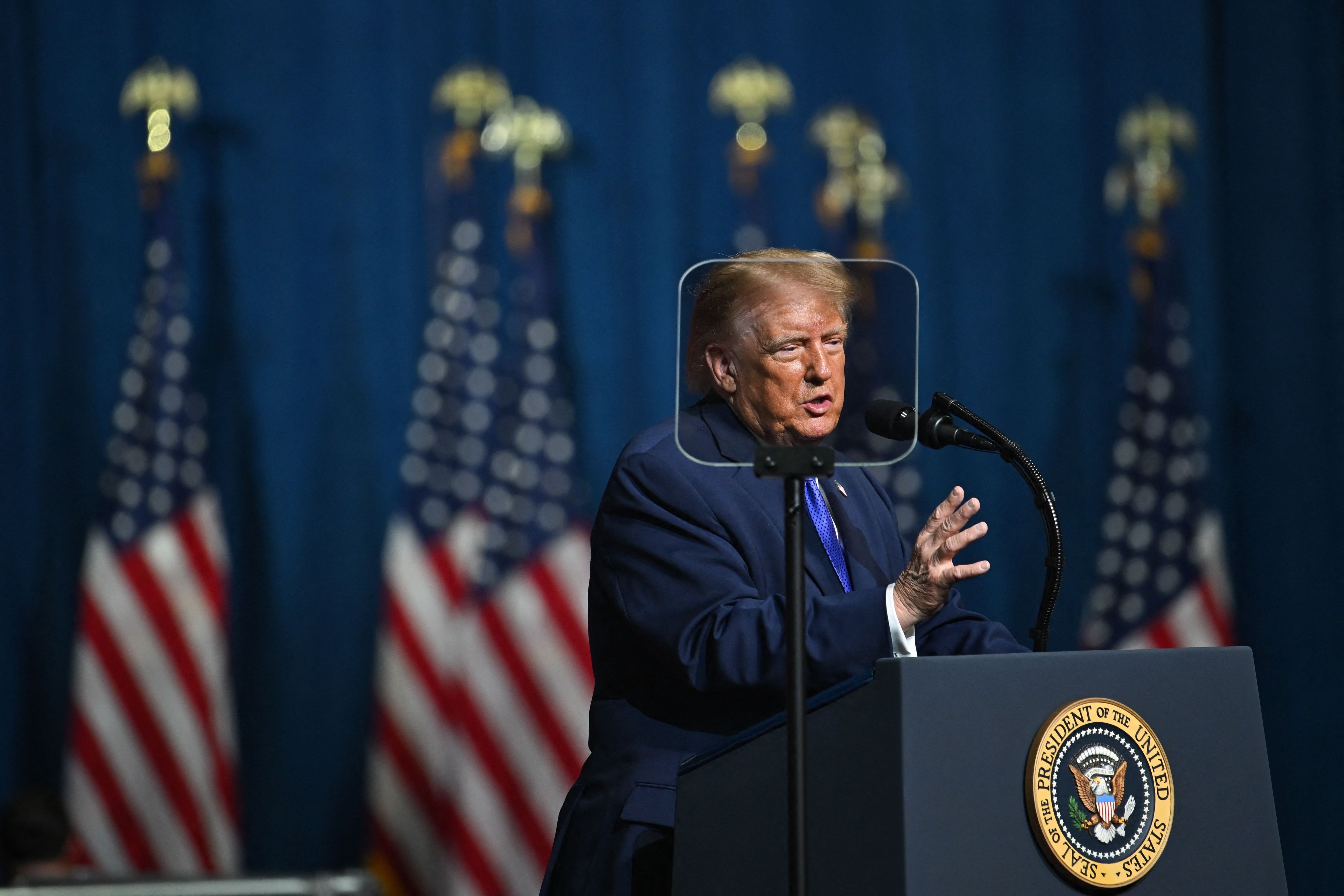 Ein Mann spricht bei einer Rede am Rednerpult mit US-Präsidialsiegel, US-Flaggen im Hintergrund.