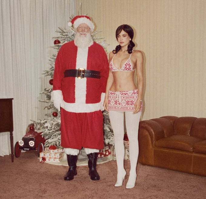 Ein Weihnachtsmann steht neben einer Frau in festlicher SKIMS-Unterwäsche vor einem Weihnachtsbaum.