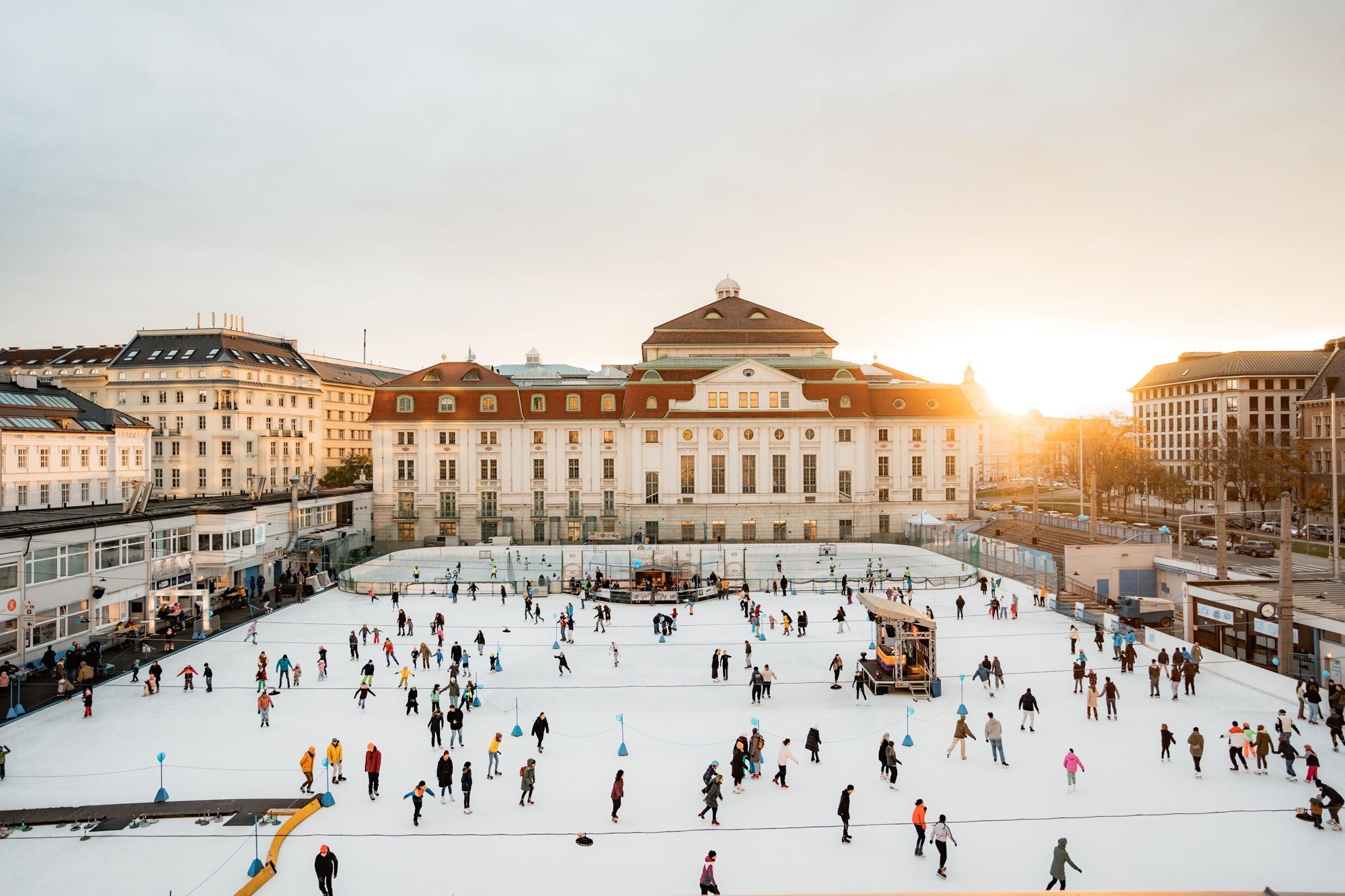 Viele Menschen laufen auf einer großen Eislaufbahn vor einem historischen Gebäude in Wien.