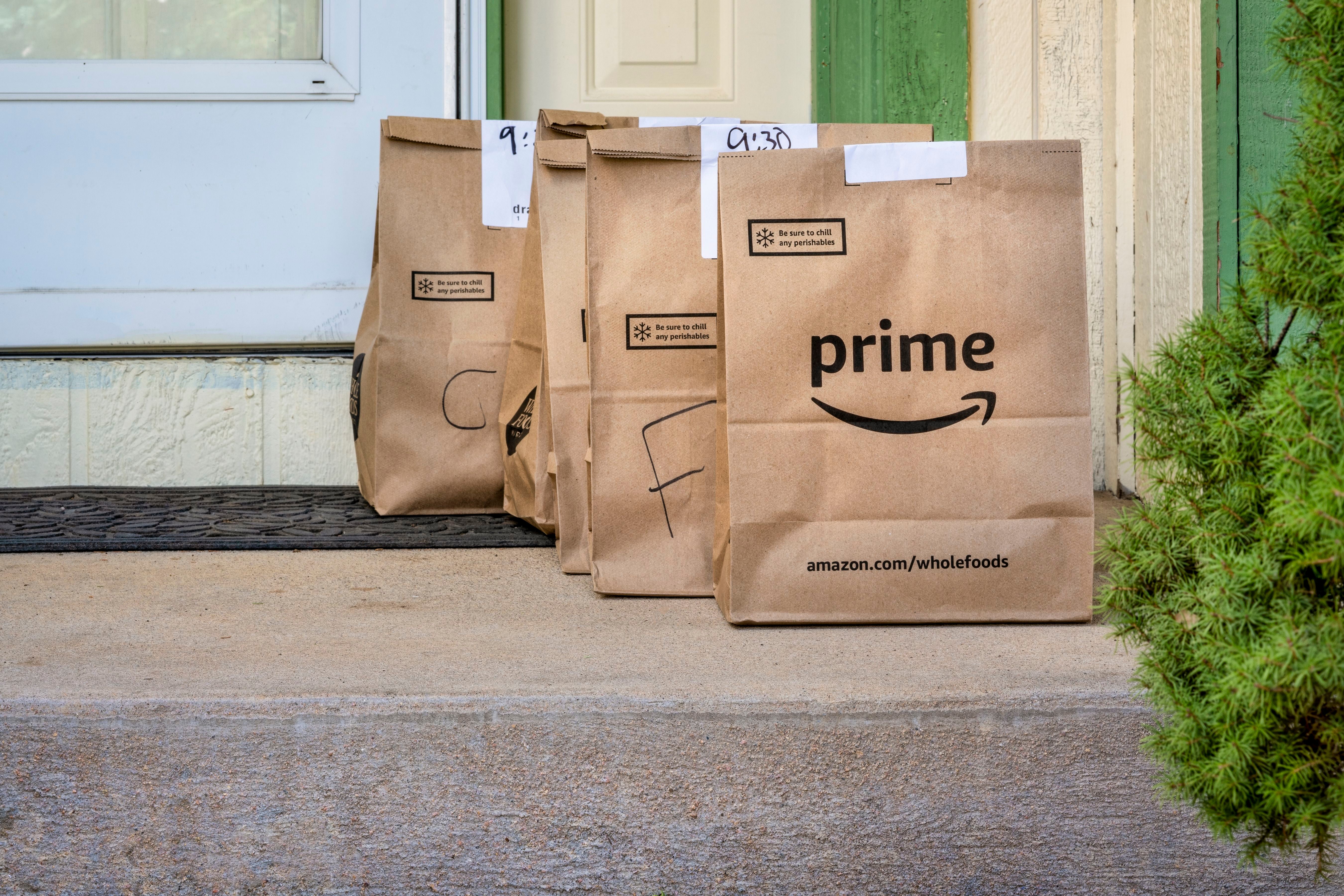 Drei Tüten mit Amazon Prime Lebensmittellieferung stehen vor einer Haustür.